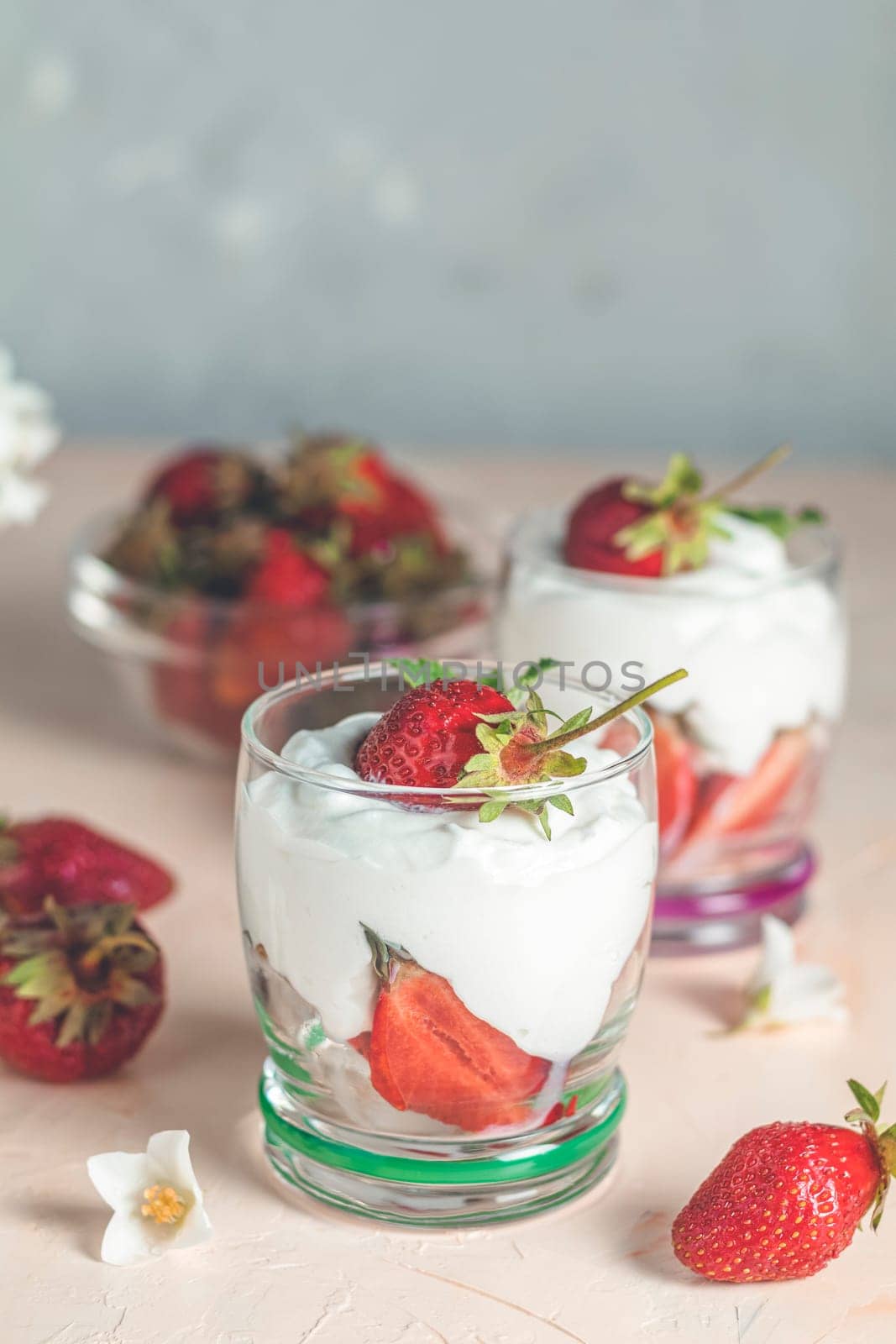 Two glasses with layered dessert of strawberries and cream cheese decorated with fresh strawberries and jasmine flowers on pink background