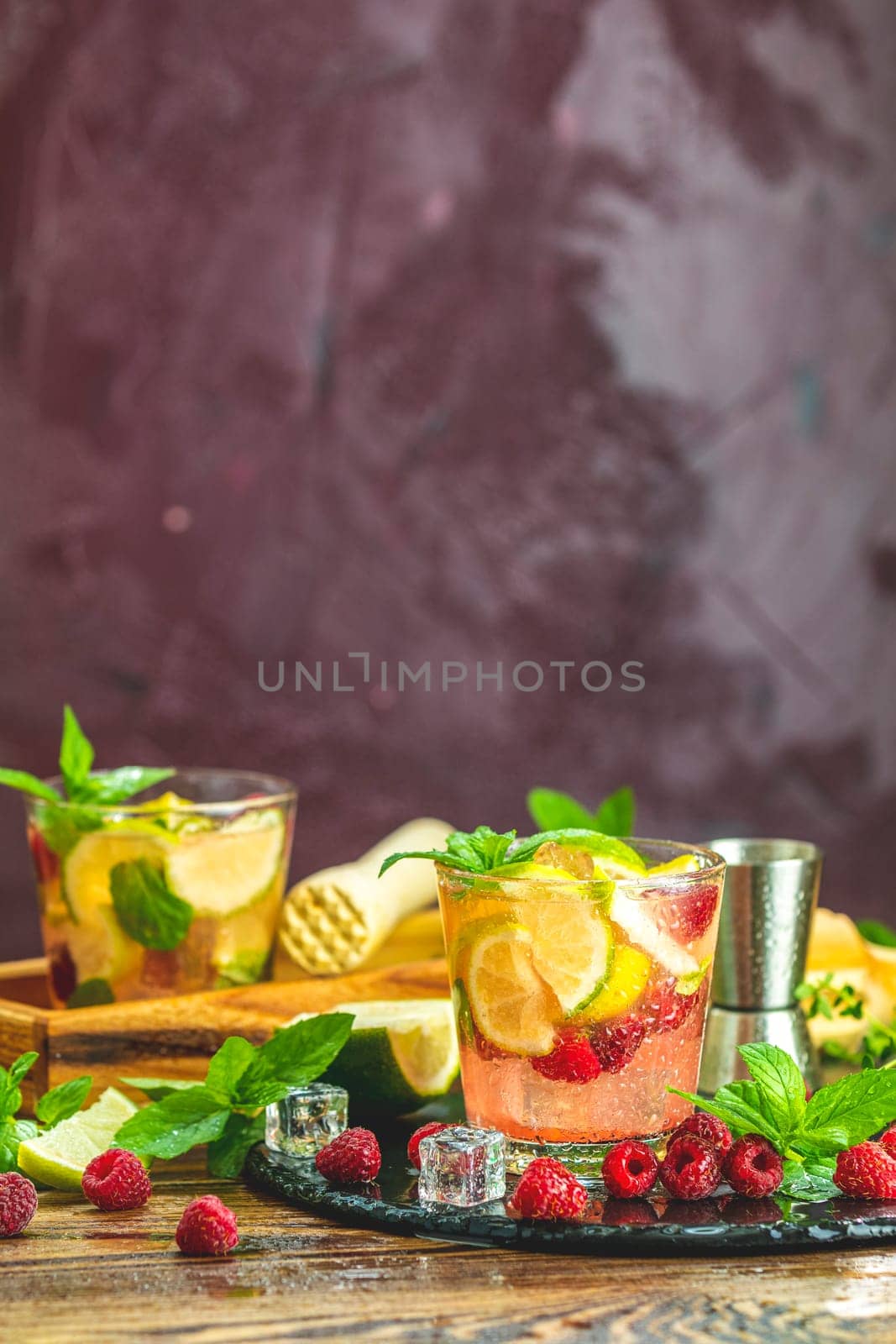 Two glasses of vibrant pink raspberry and lime cocktail garnished with fresh mint and ice cubes, creating a refreshing summer drink