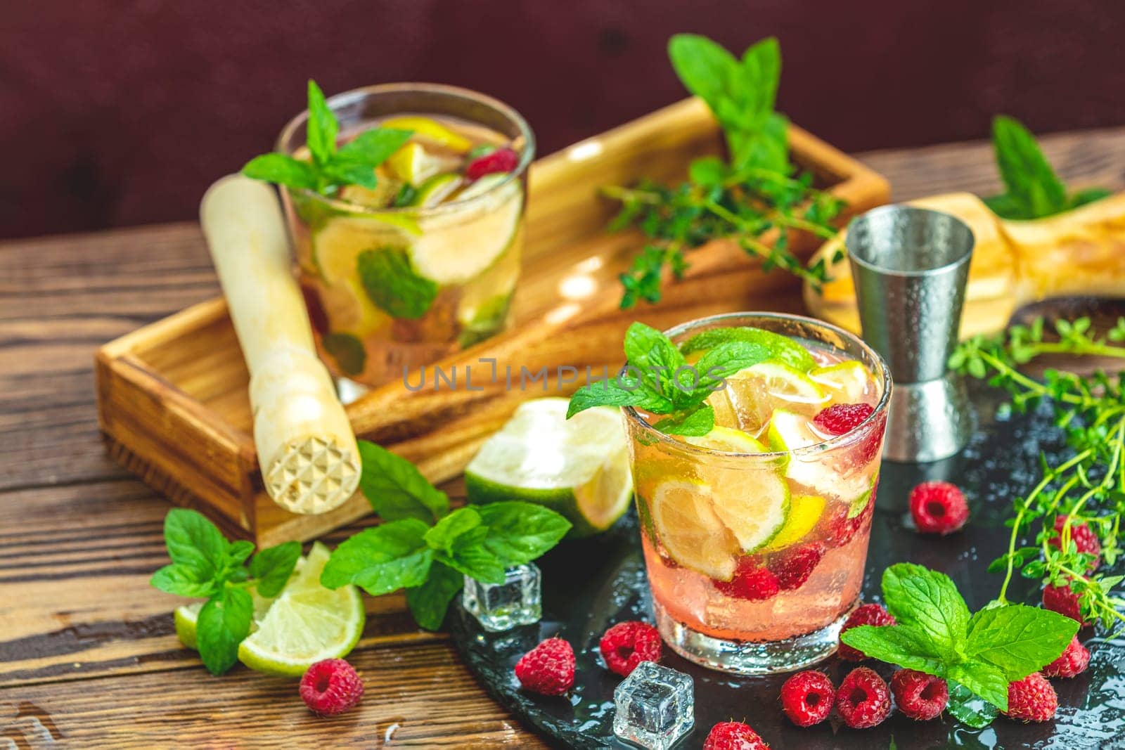 Refreshing summer cocktail with raspberries, lime, mint, ice and a muddler on a wooden table