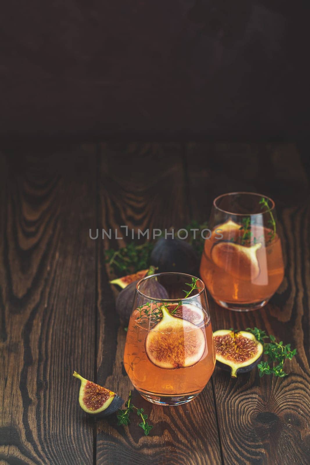 Two refreshing pink cocktails garnished with fresh figs and thyme sprigs sit on a dark wooden table, creating a vibrant and inviting scene