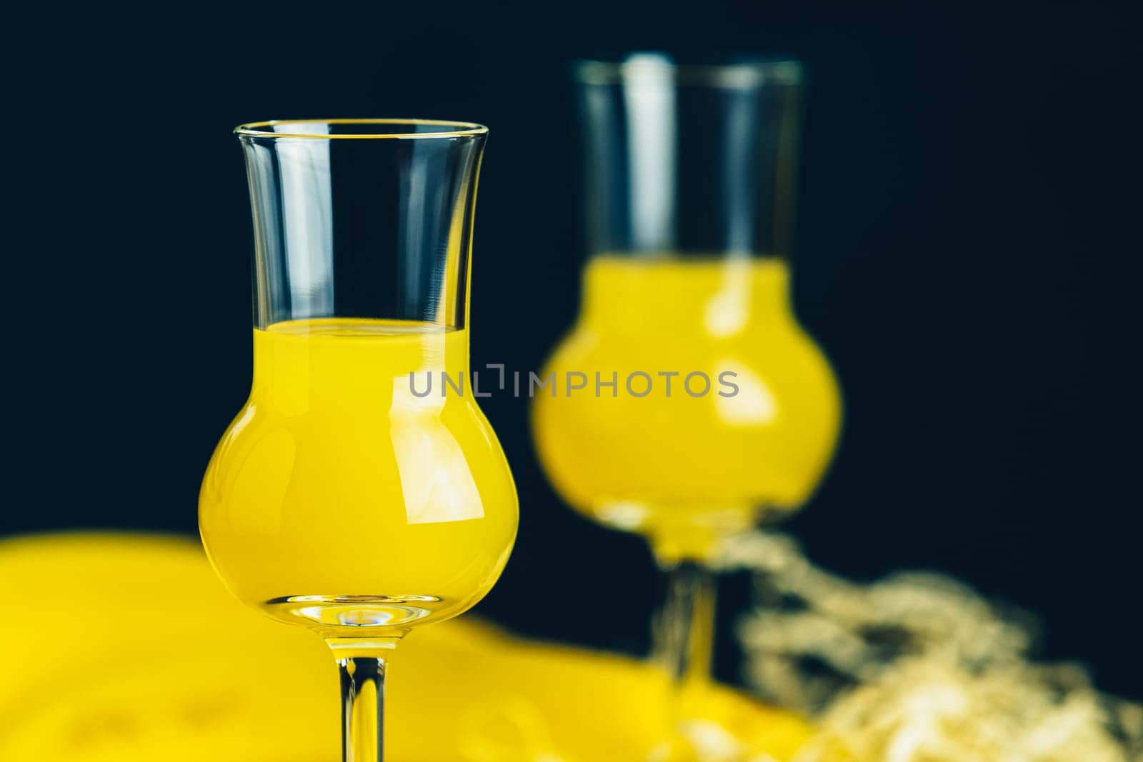 Two glasses filled with yellow liquor stand on a table with a dark background, creating a vibrant and inviting scene