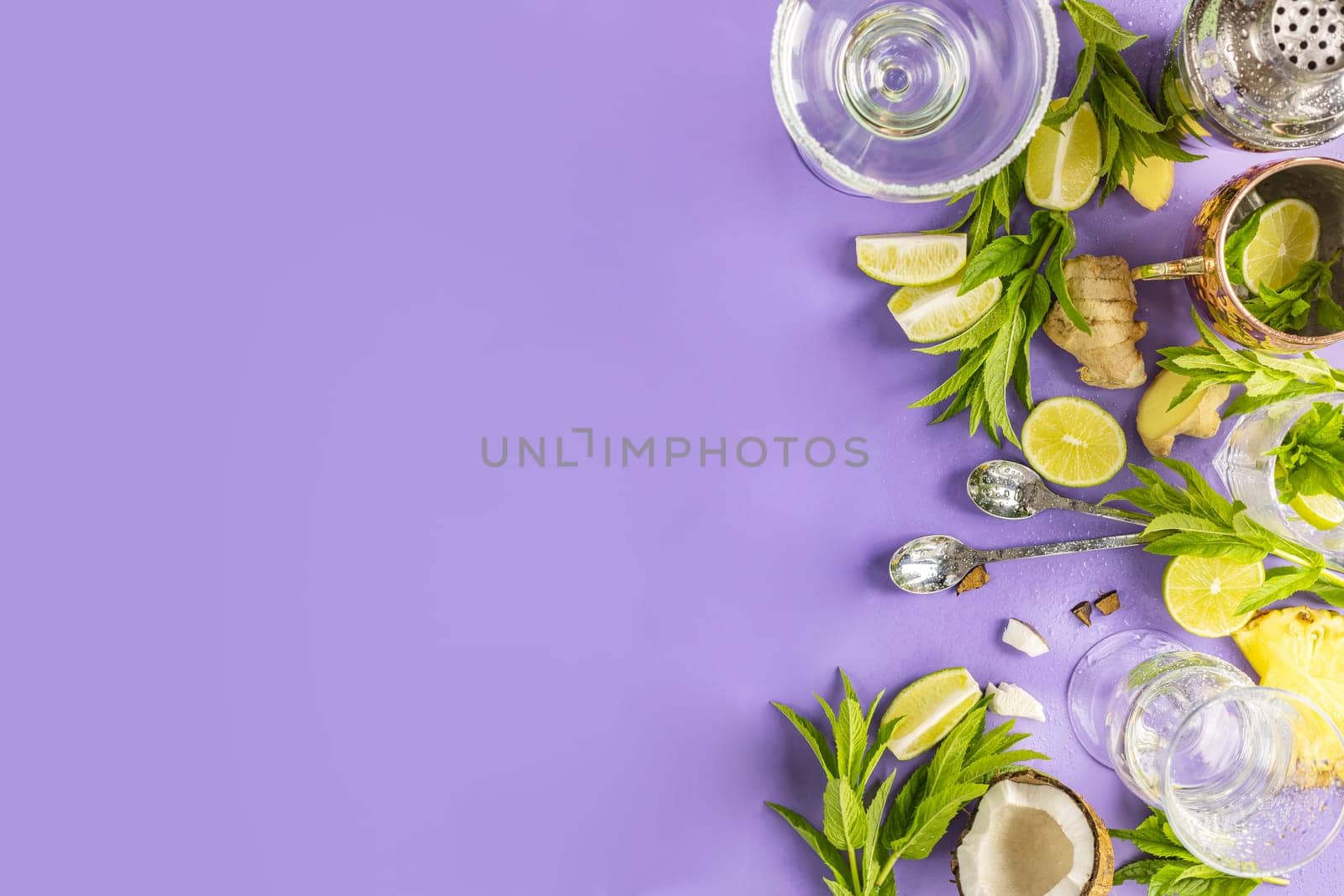 Fresh mint, lime, ginger, coconut, and pineapple arranged against a purple background with cocktail shaker and glasses for a vibrant summer drink