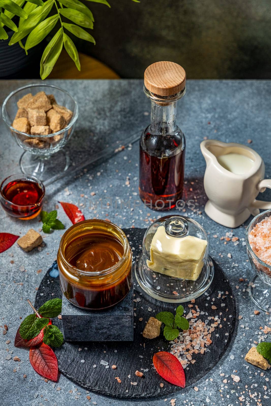 Preparing salted caramel sauce with butter, cream, brown sugar, fleur de sel and maple syrup on dark gray kitchen table