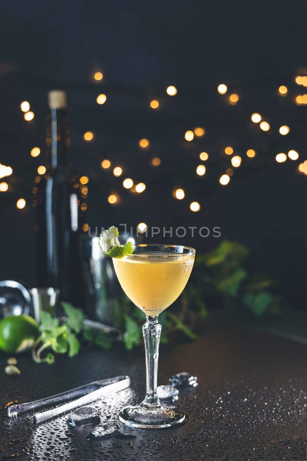 Refreshing cocktail served in elegant glass, garnished with lime and mint, sits on wet countertop against bokeh background