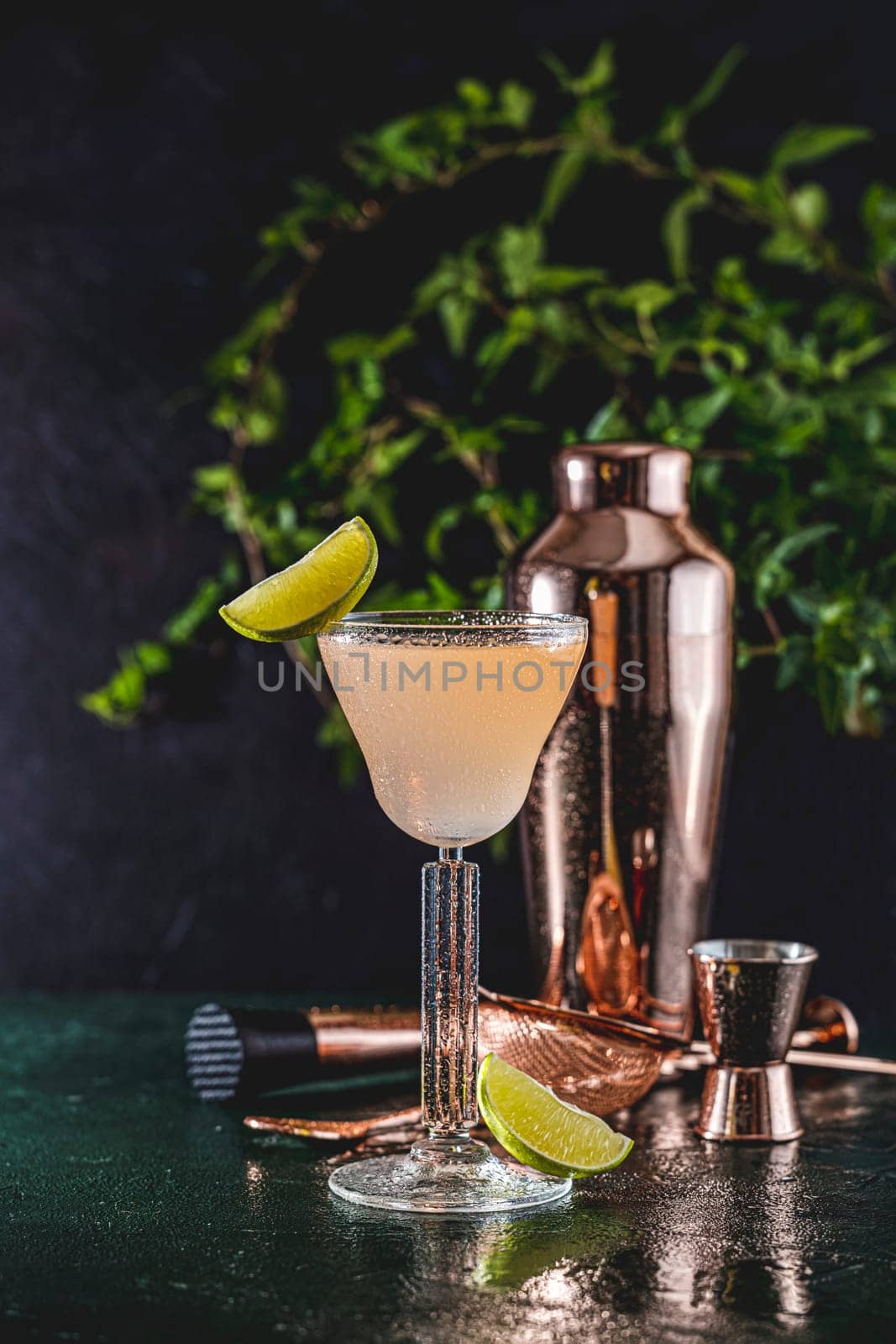 Vibrant cocktail, garnished with a lime wheel, sits on a wet bar top amidst copper bar tools, creating a refreshing and sophisticated atmosphere