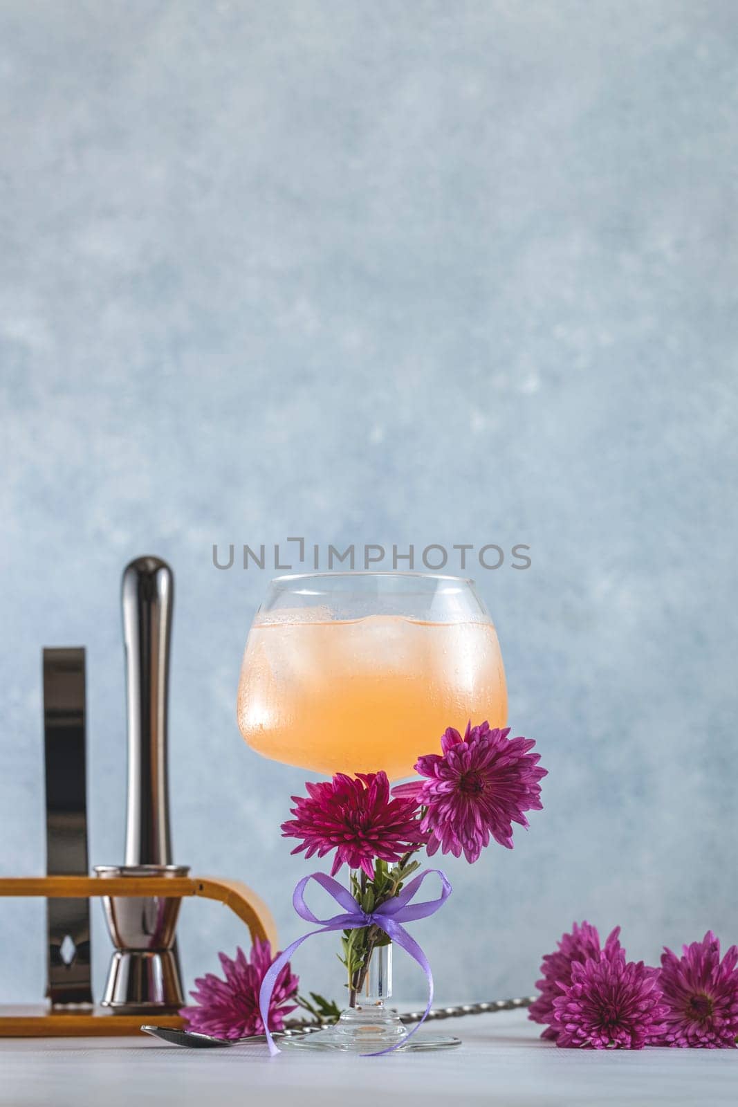 Glass with pink cocktail decorated with fresh flowers and bar tools in the background, creating a stylish and refreshing scene