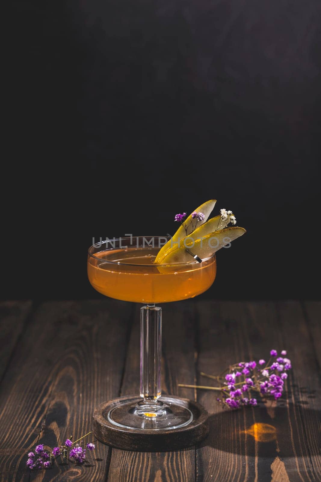 Pear cocktail garnished with pear slices and small flowers, served in an elegant coupe glass on a rustic wooden table