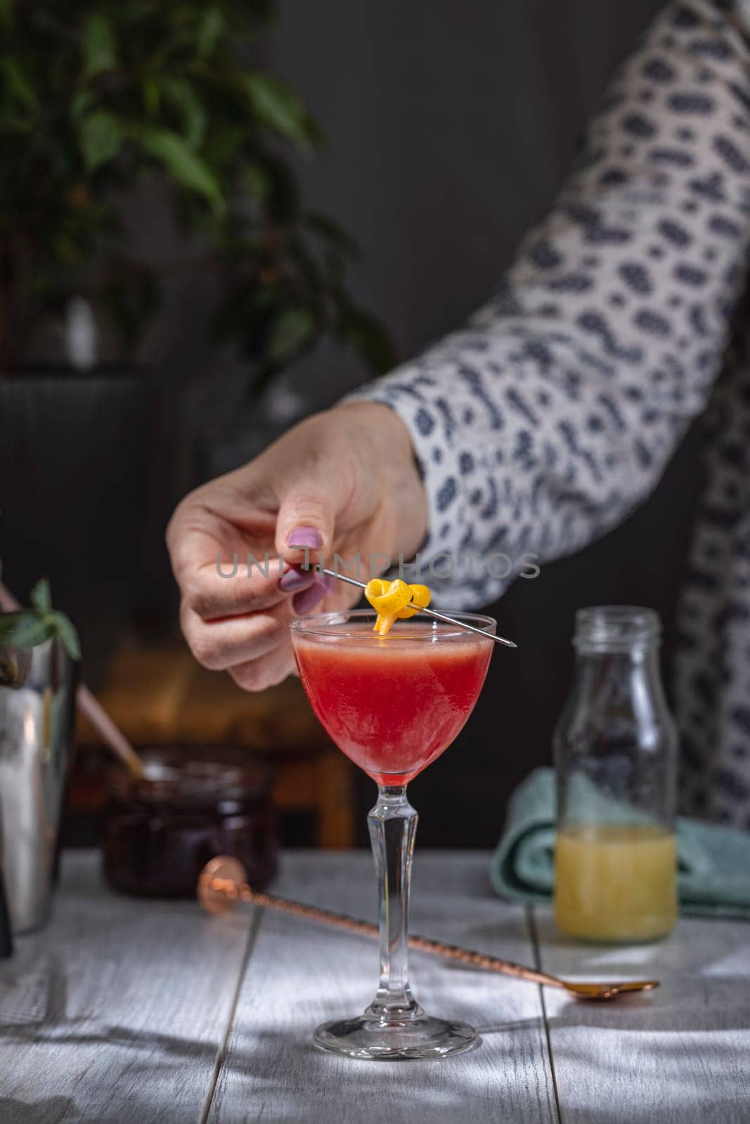 Bartender adding a lemon twist garnish to a vibrant red cocktail in a coupe glass, showcasing the art of cocktail making