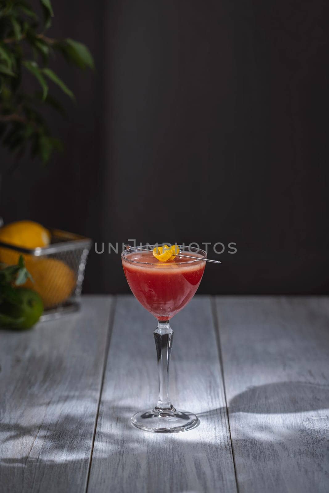 Refreshing cosmopolitan cocktail served in a coupe glass, garnished with a lemon twist, on a white wooden table against a dark background