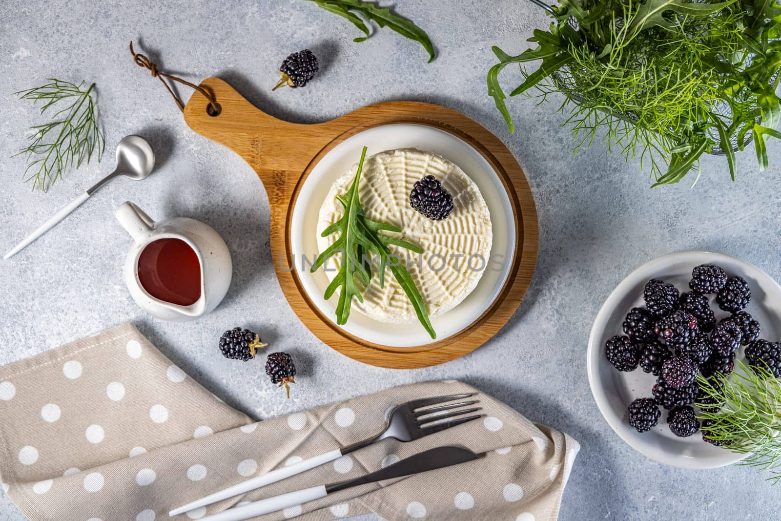 Top view of fresh round cheese with blackberries and rocket salad on wooden board, served with berry sauce, healthy eating concept