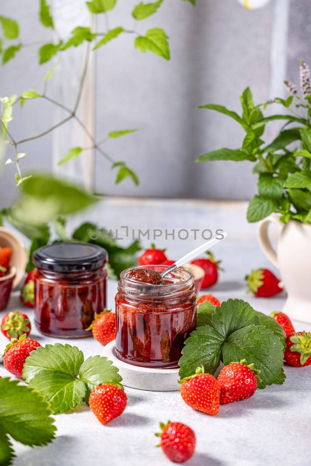 Two glass jars filled with homemade strawberry jam, accompanied by fresh strawberries, leaves, and a spoon, creating a vibrant and appetizing scene