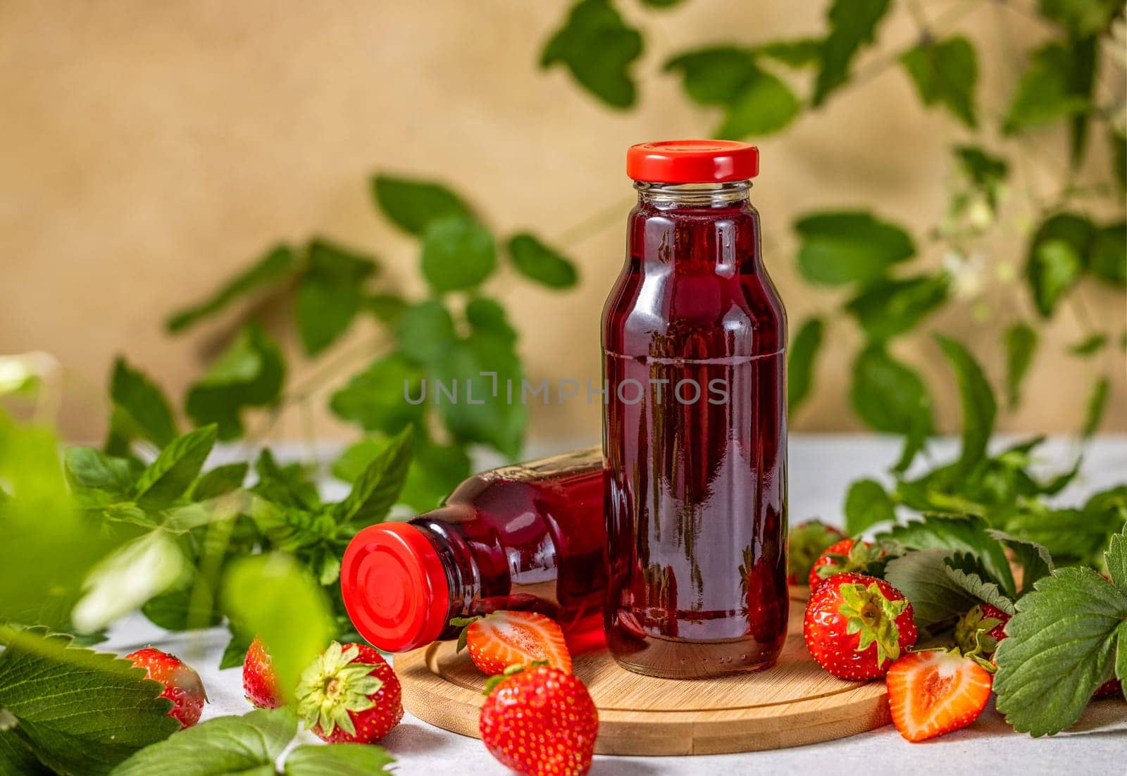 Two bottles of refreshing strawberry juice sit on a wooden board, surrounded by fresh strawberries and mint leaves, creating a vibrant and healthy scene