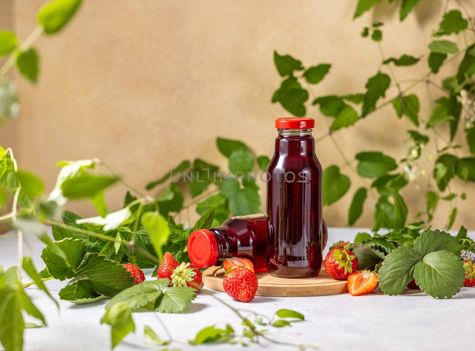 Two bottles of refreshing strawberry juice sit on a wooden coaster, surrounded by fresh strawberries and lush green leaves, creating a vibrant and healthy image