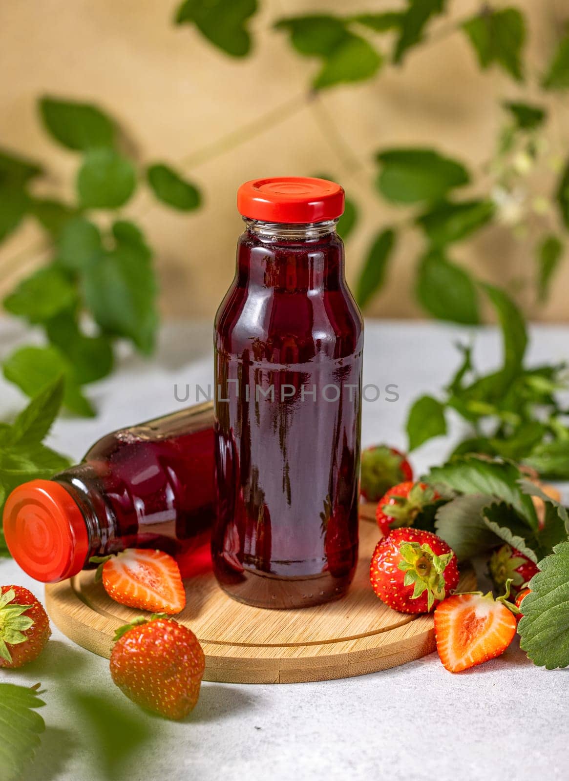 Two bottles of strawberry juice are standing on a wooden board with fresh strawberries and leaves, creating a refreshing summer scene