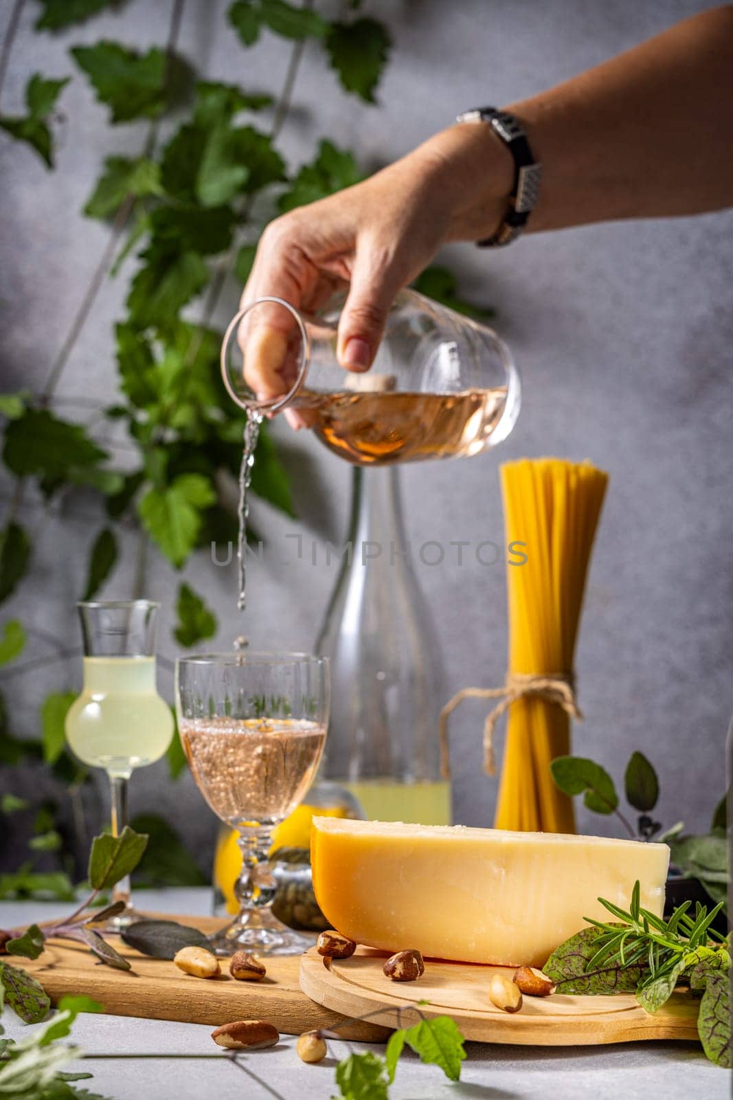 Rose wine being poured into a glass, accompanied by cheese, pasta, nuts, and herbs, creating an elegant culinary scene