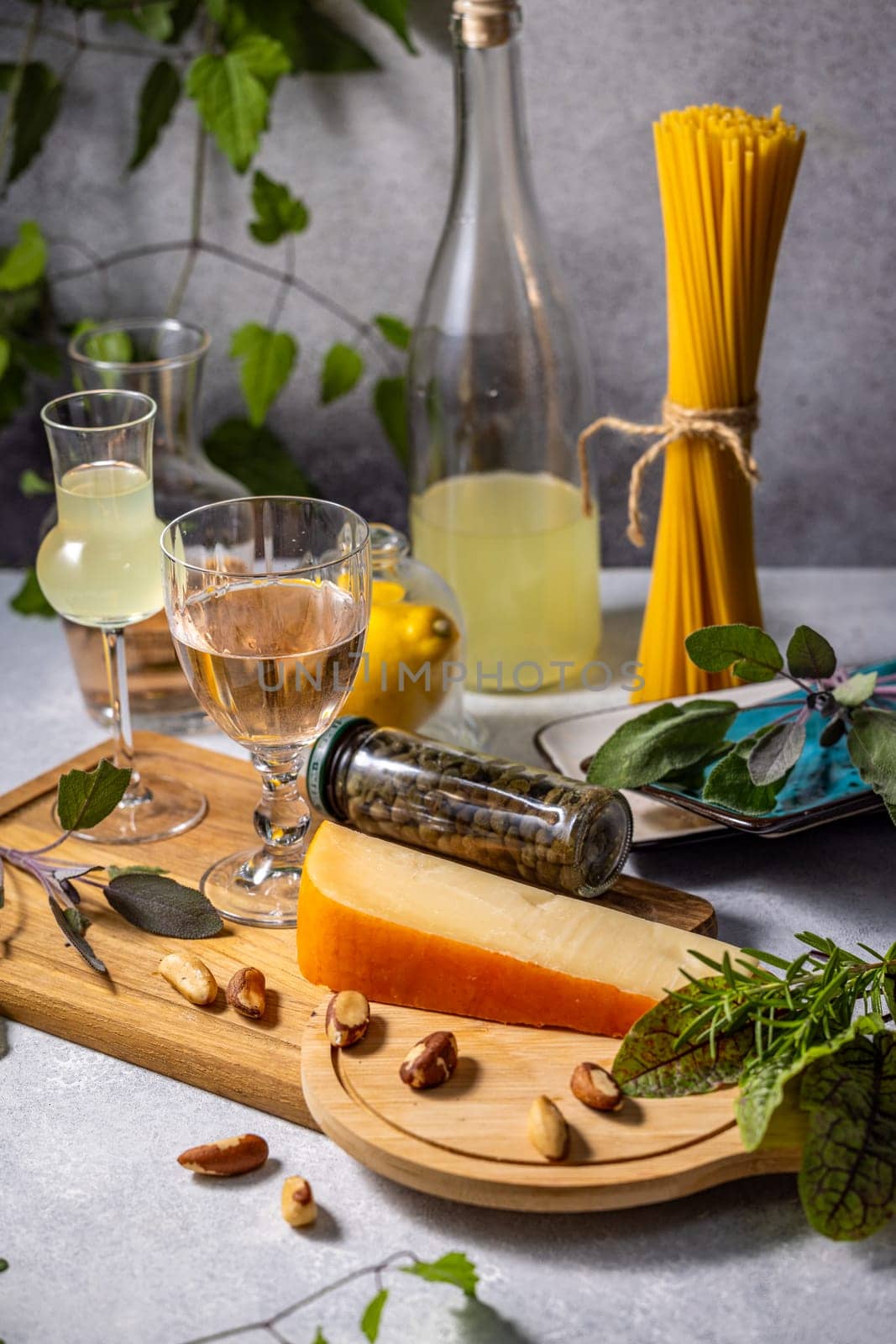 Italian culinary still life featuring cheese, pasta, wine, limoncello, capers, herbs, and brazil nuts