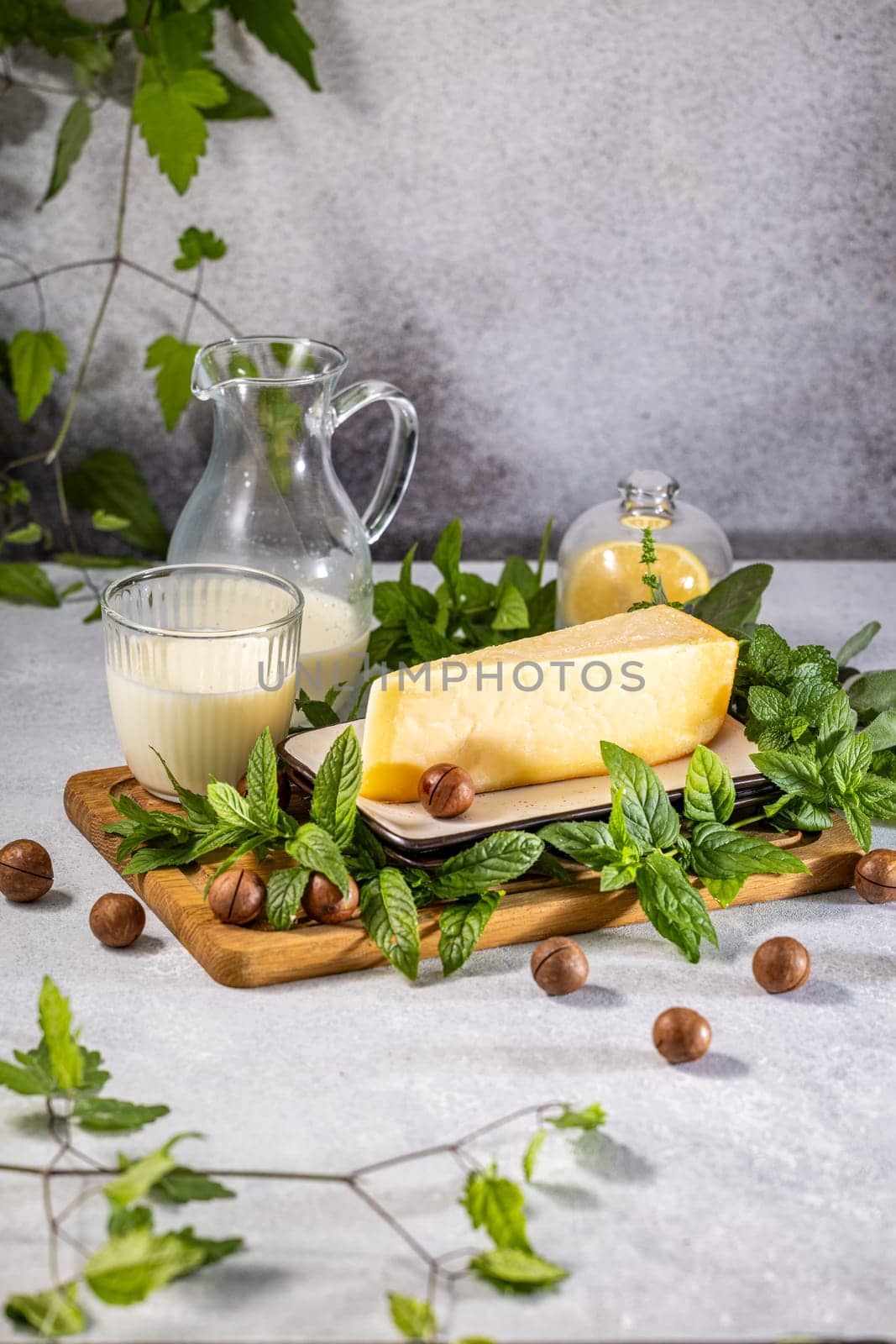 Hard cheese, milk, macadamia nuts, and mint leaves are arranged on a wooden board, creating a visually appealing and flavorful composition