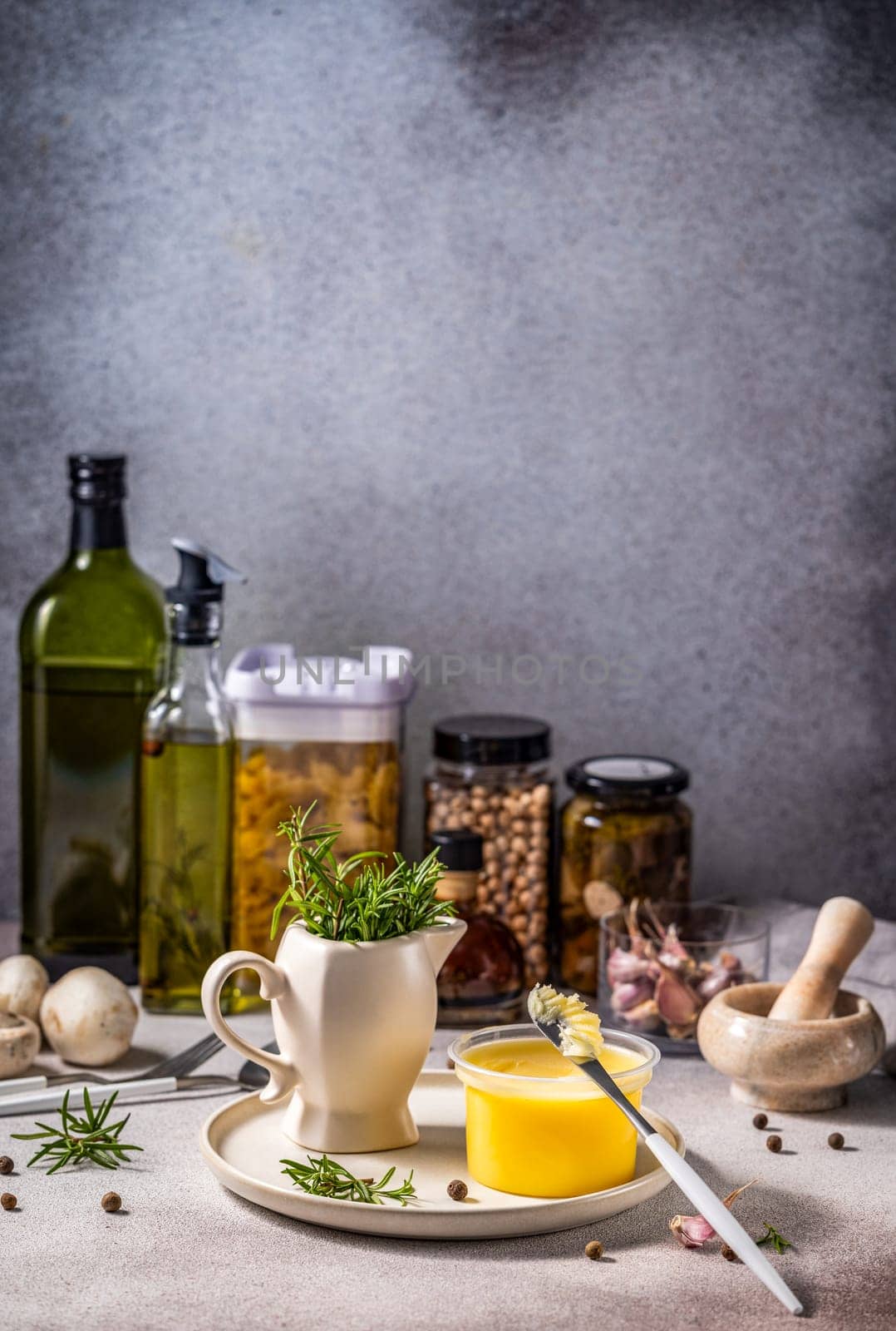 Ghee butter, rosemary, olive oil, pasta, chickpeas, spices, and other food ingredients arranged on kitchen table, creating a cozy cooking atmosphere