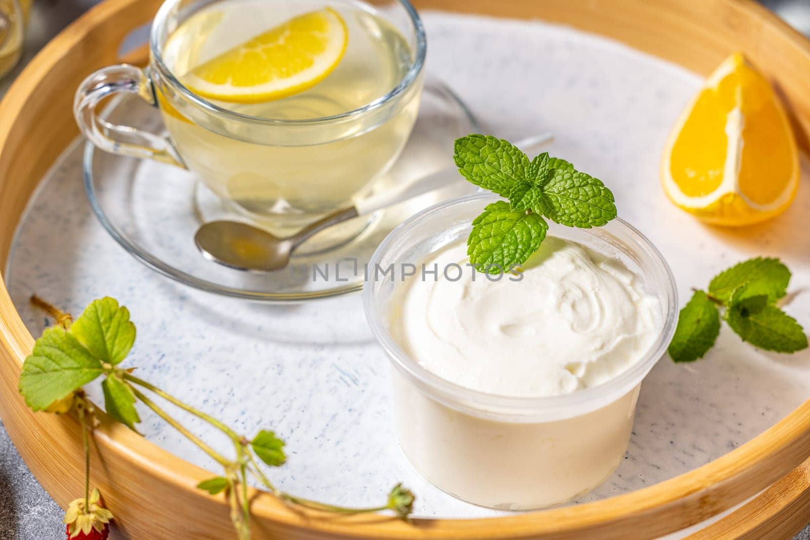 Creamy dessert with mint served on wooden tray with lemon tea, orange slice and wild strawberry twig
