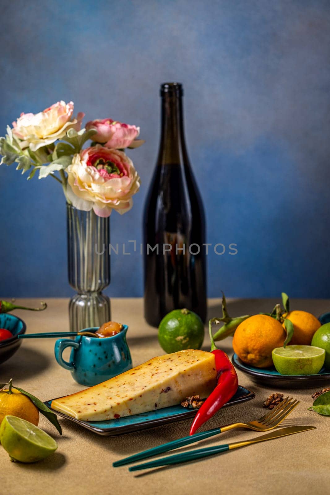 Wedge of gourmet cheese resting on a plate with chili pepper, fresh fruits, wine, and flowers, creating an elegant dining scene