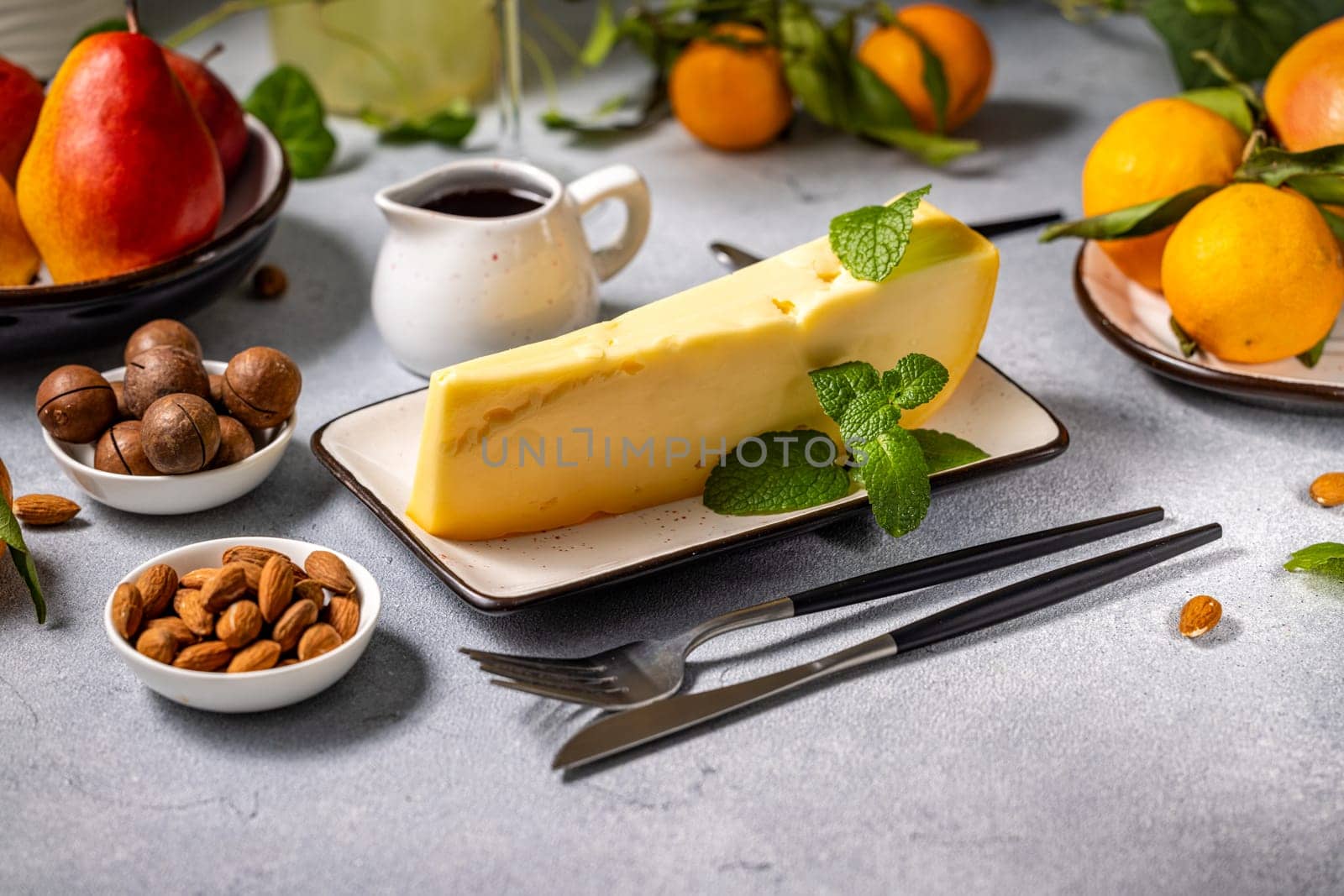 Slice of gourmet cheese served with fresh mint, accompanied by fruits, nuts, and a small pitcher of syrup, creating an elegant table setting