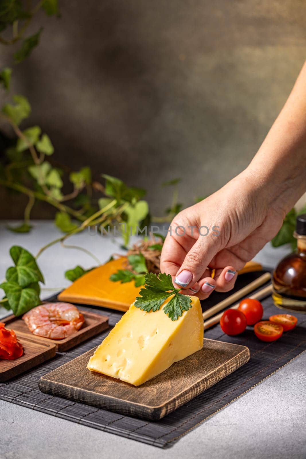 Chef garnishing a wedge of cheese with fresh parsley on a wooden board, preparing a gourmet dish with various ingredients