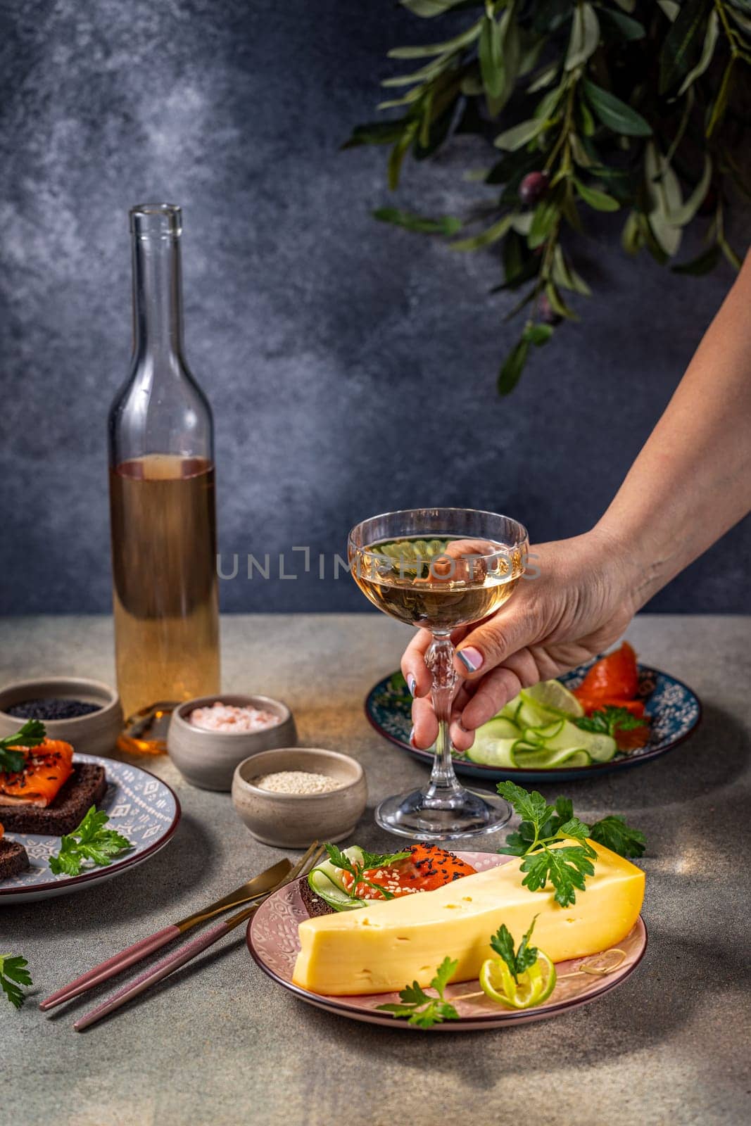 Hand holding a glass of white wine with gourmet cheese and salmon appetizers, creating an elegant and appetizing scene