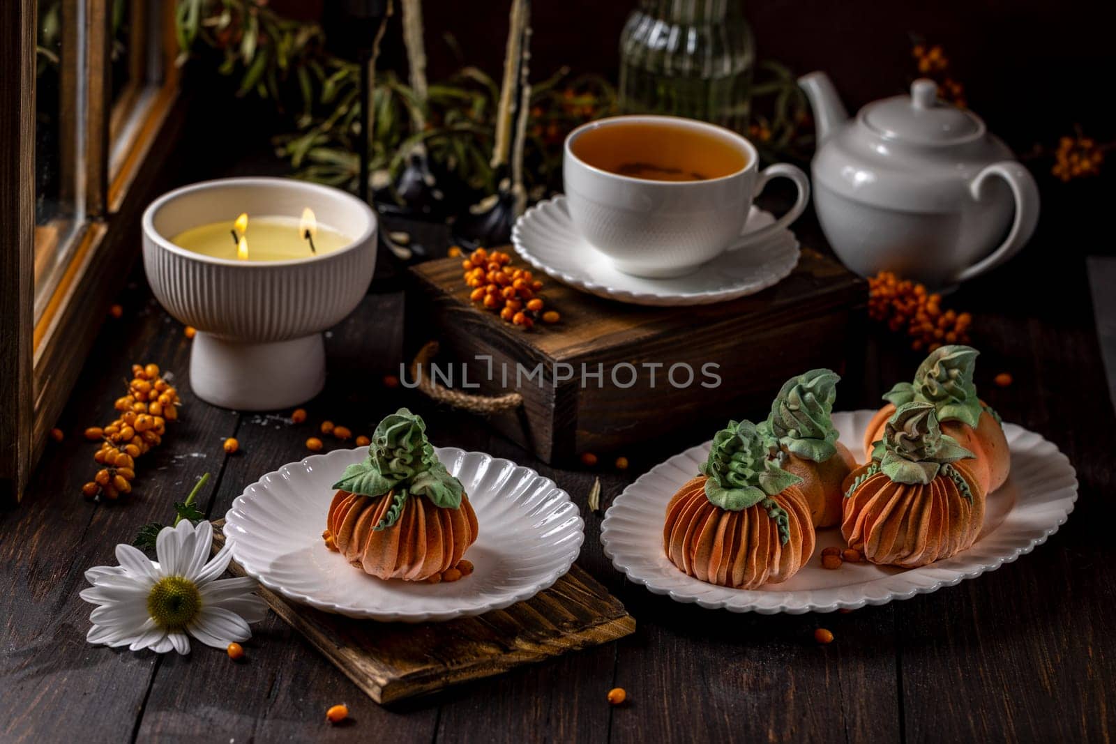 Delicious pumpkin shaped desserts served with tea, creating a warm and inviting autumn atmosphere by the candlelight