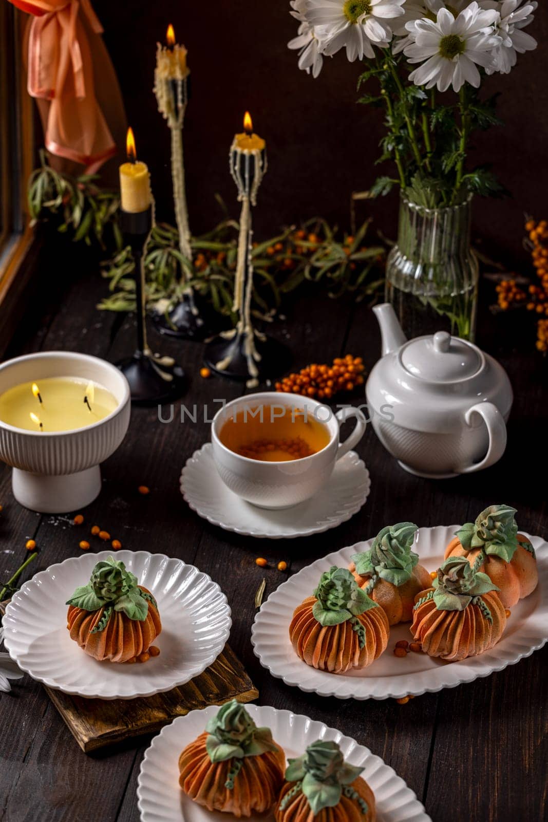 Delicious pumpkin shaped desserts served with tea on a table adorned with candles and flowers, evoking a warm and inviting autumnal ambiance