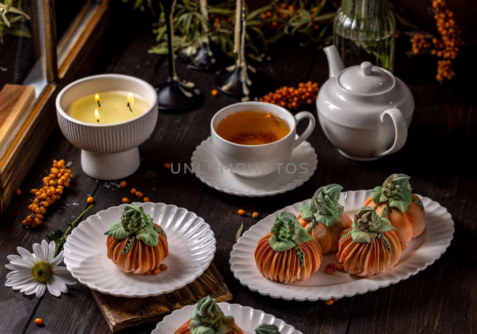 Delicious pumpkin shaped desserts served with tea and a lit candle, creating a cozy and inviting atmosphere for autumn