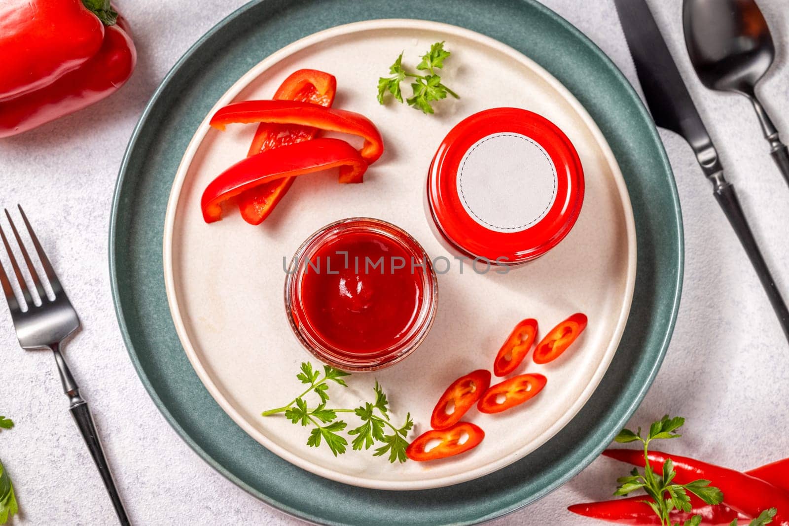 Red pepper relish in small glass jars, accompanied by fresh red chili pepper slices and parsley sprigs, served on a plate