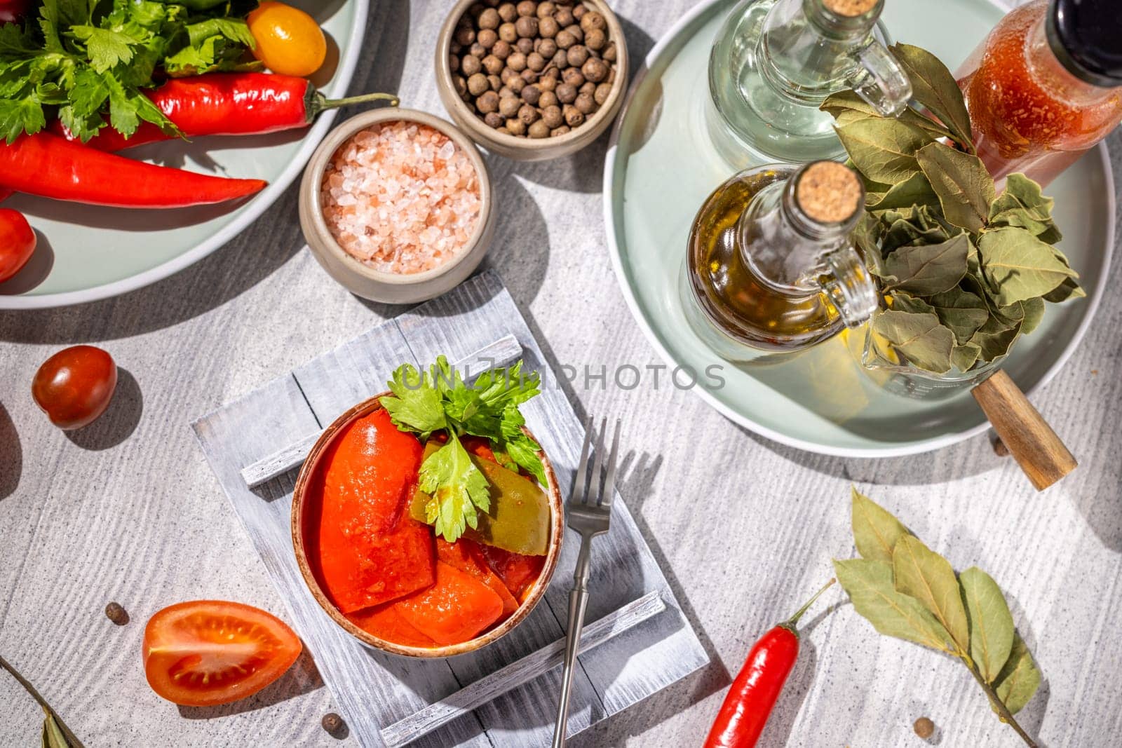 Pickled red bell peppers in a wooden bowl, garnished with fresh parsley, fresh tomatoes, chili peppers, spices, and olive oil