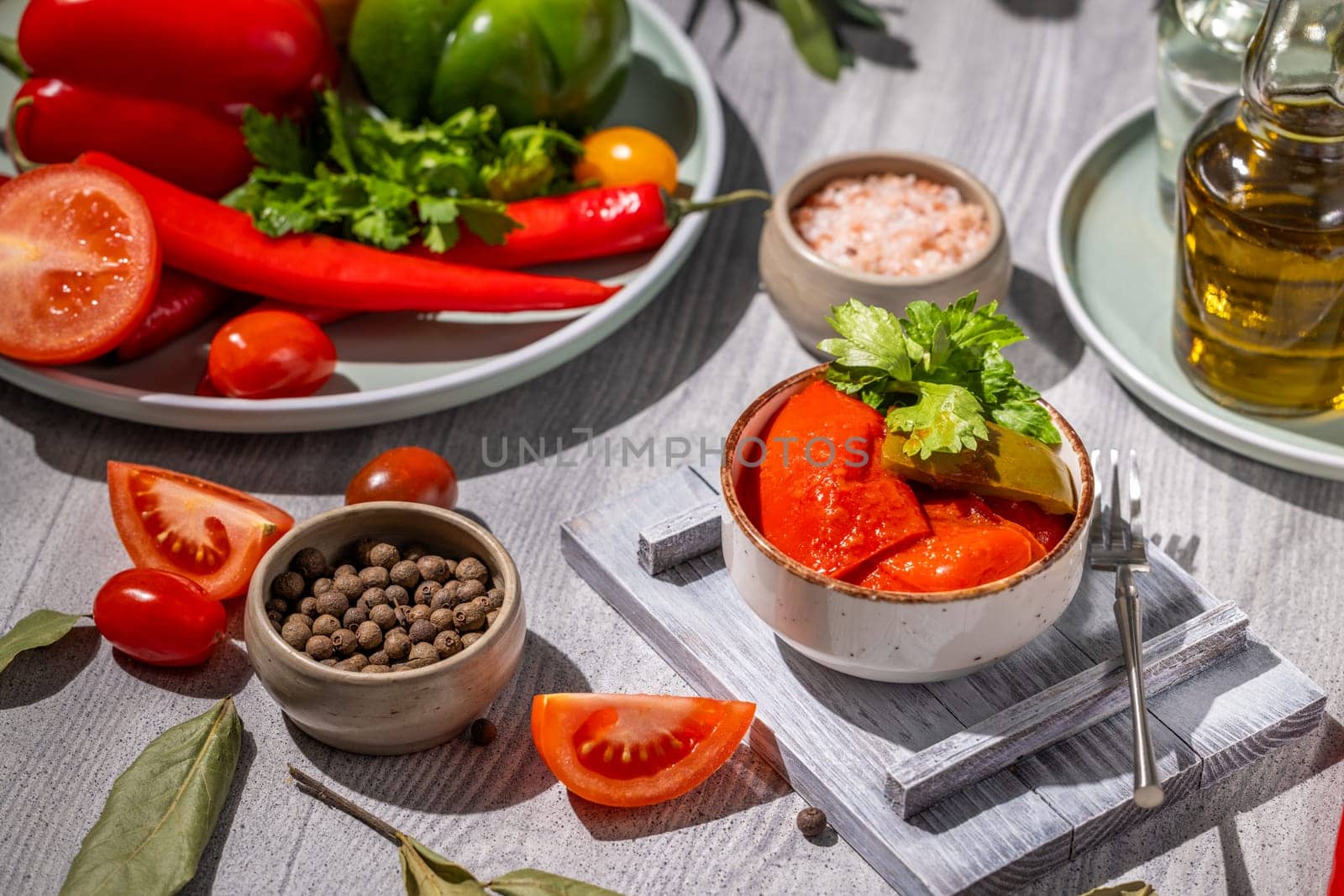 Small bowl of pickled red pepers, accompanied by fresh vegetables, spices, and olive oil, showcasing a colorful and appetizing culinary arrangement