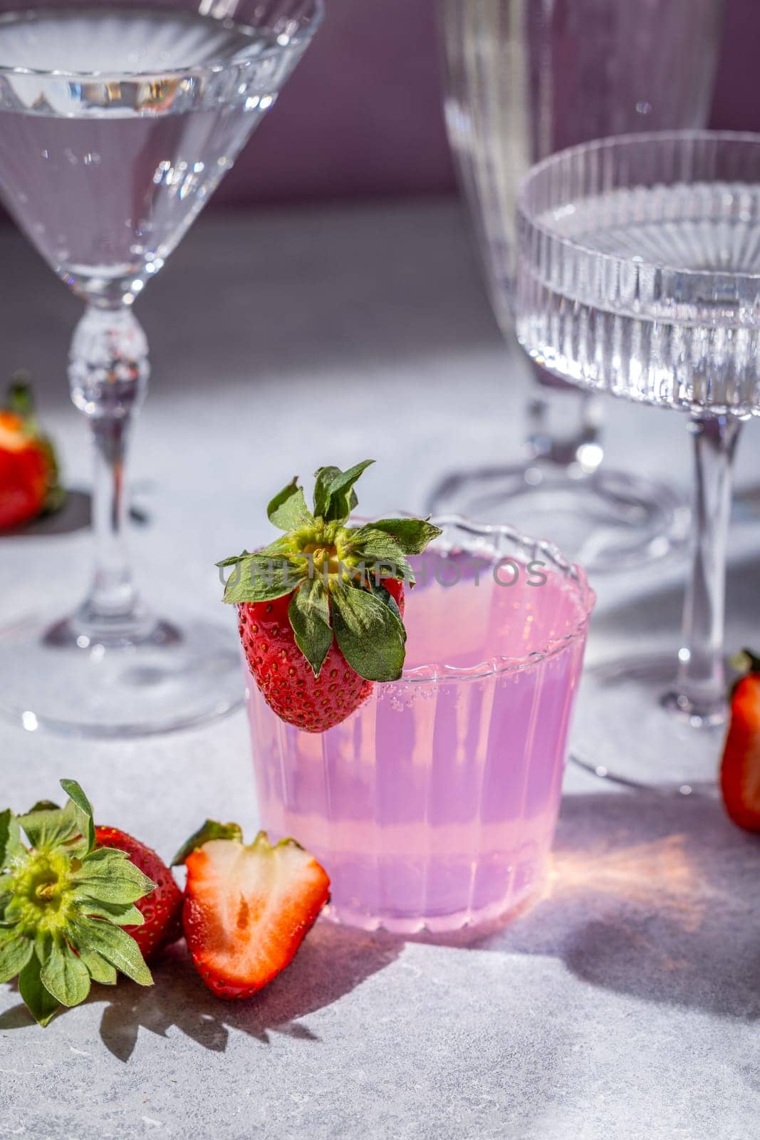 Vibrant pink strawberry cocktail, garnished with fresh strawberries, served in a stylish glass alongside elegant glassware