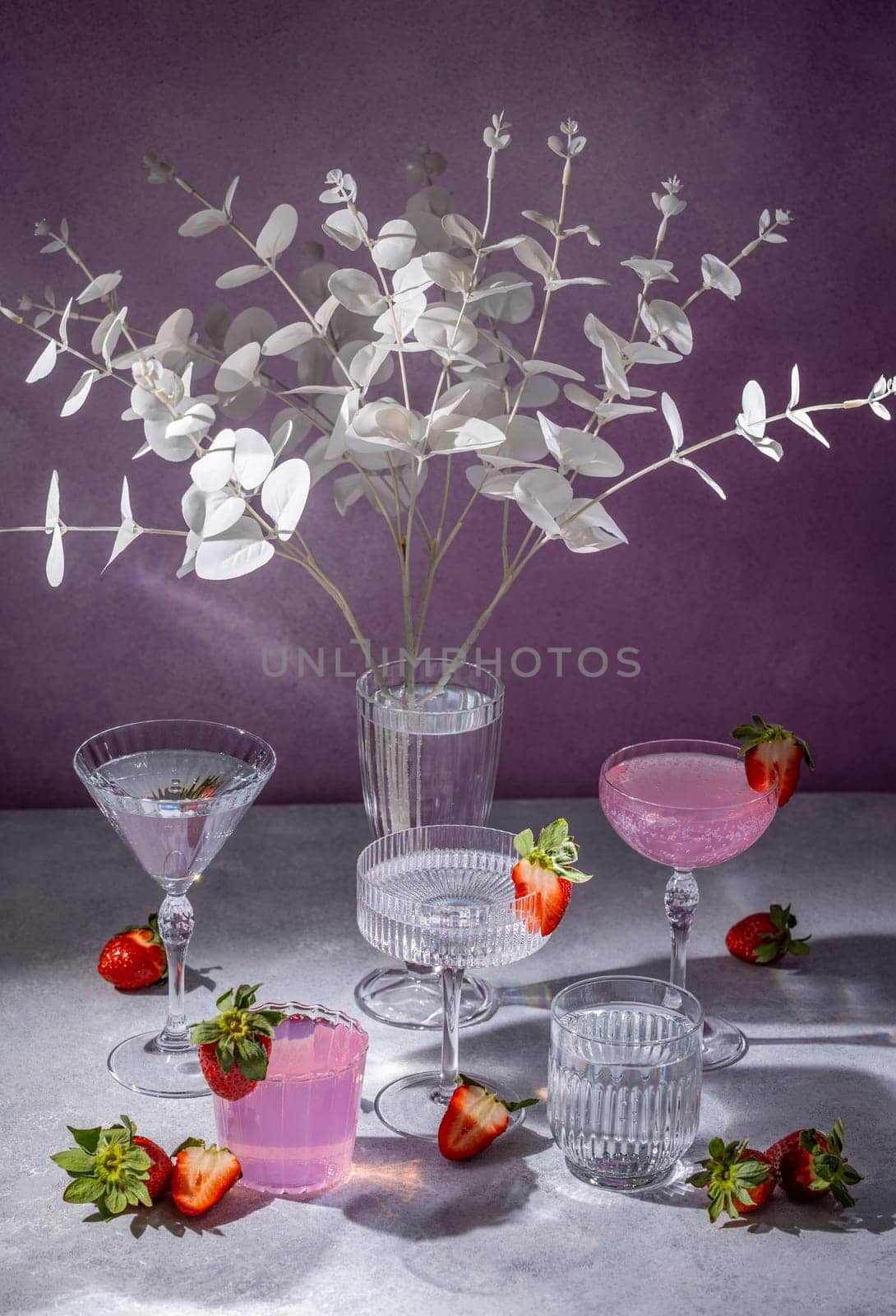Crystal glasses filled with pink cocktails and fresh strawberries, arranged elegantly on a table with white eucalyptus branches