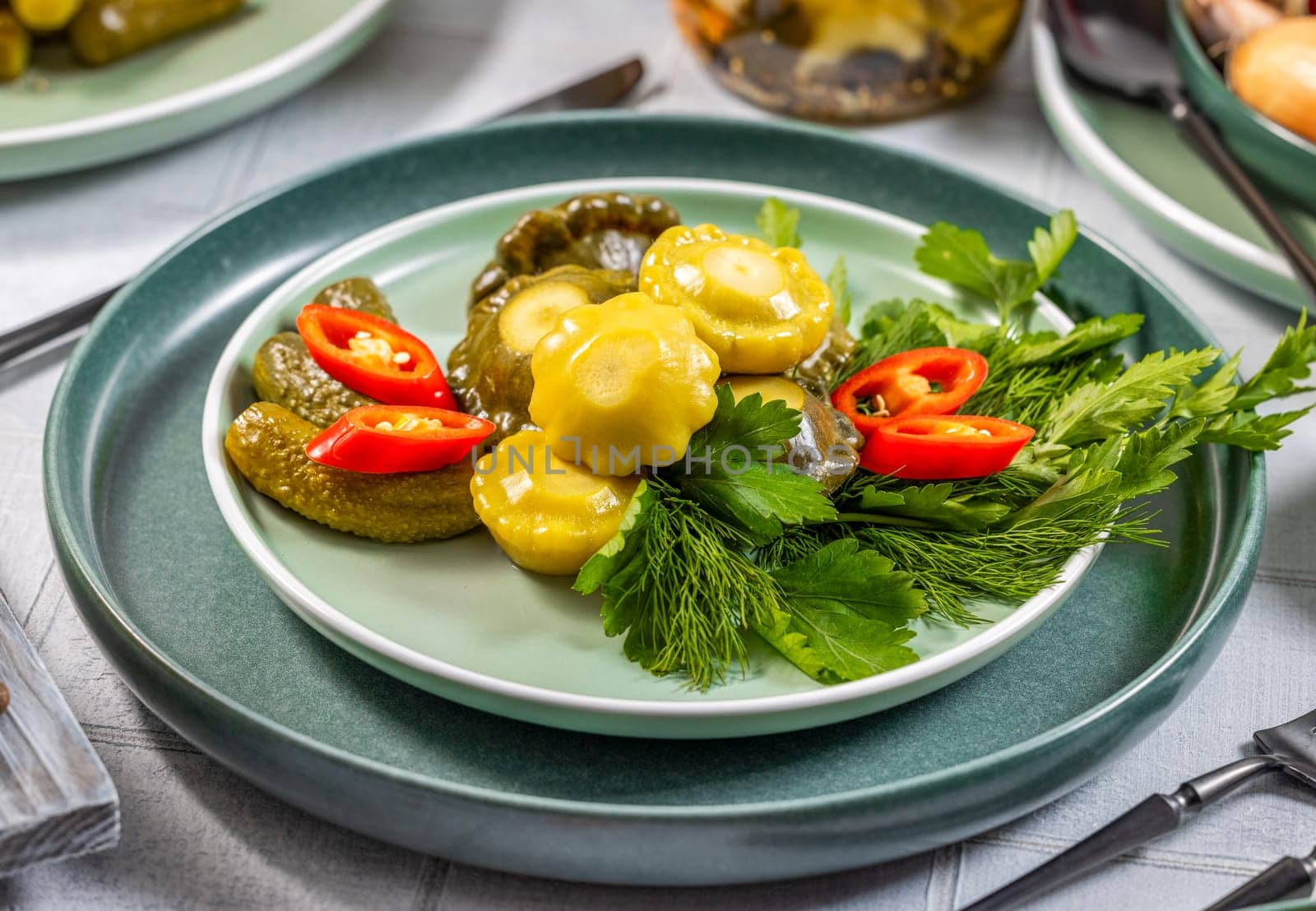 Serving plate with pickled pattypan squash and gherkins, garnished with fresh dill, parsley, and chili pepper slices