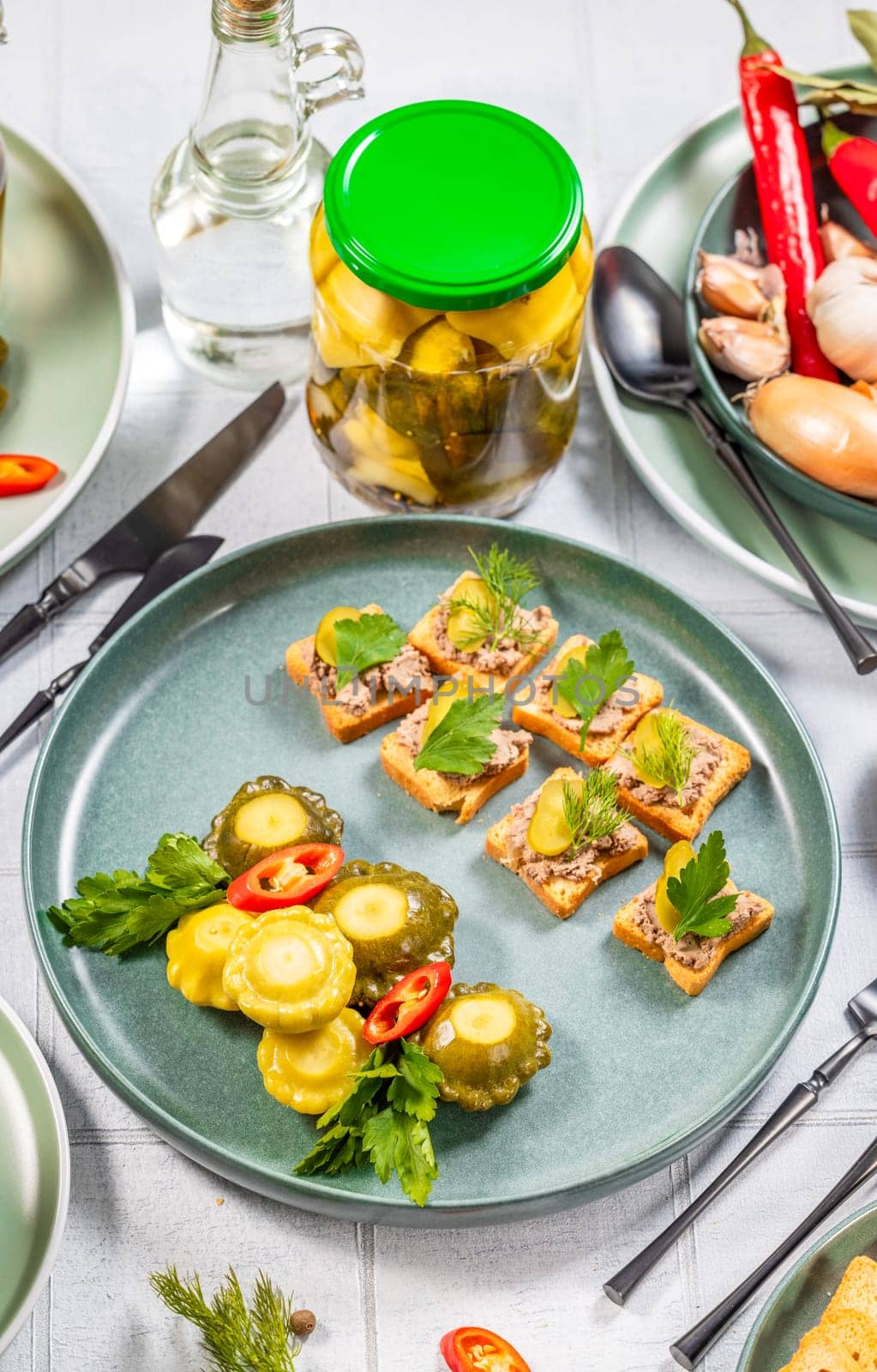Pickled pattypan squash and canape with pate, decorated with fresh herbs, served on a festive table with pickled cucumbers