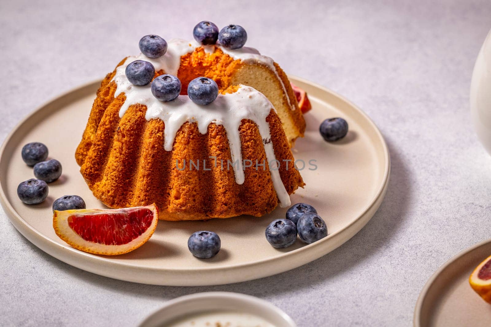 Sliced gugelhupf cake, decorated with icing, blueberries and blood orange, served on a plate