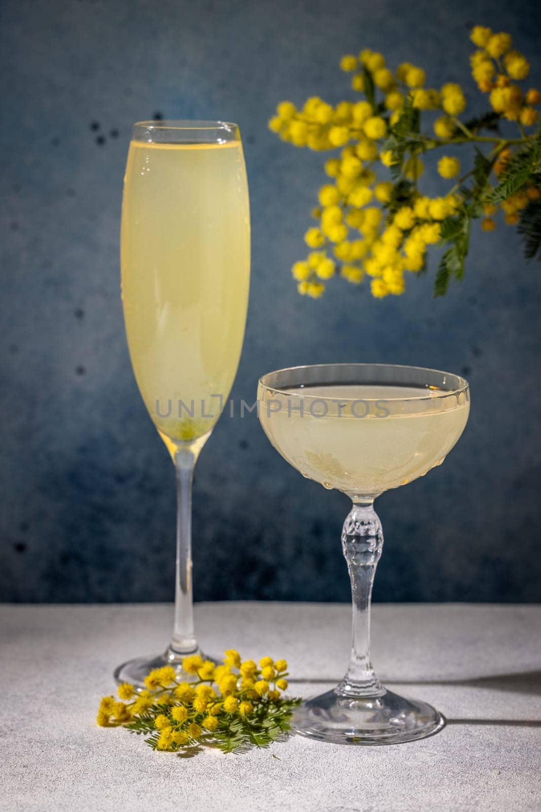 Two glasses of mimosa cocktails are garnished with mimosa flowers and placed on a table, creating a refreshing and celebratory atmosphere
