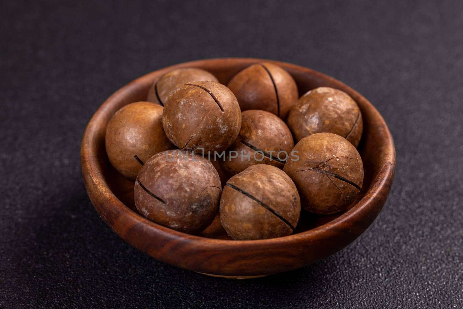 Shelled macadamia nuts sitting in small wooden bowl, creating appetizing arrangement on dark background