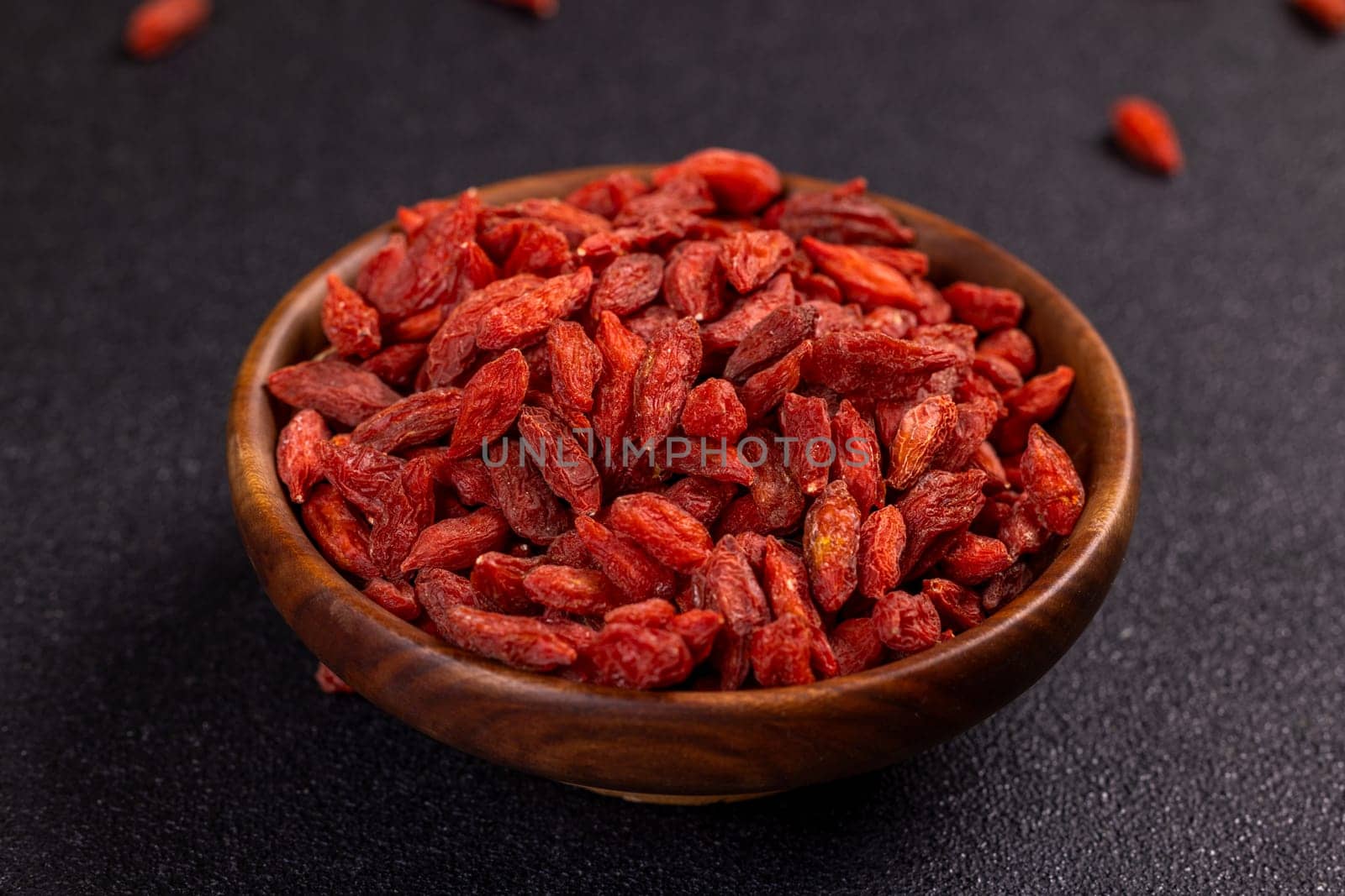 Close up of nutritious dried goji berries overflowing a wooden bowl, showcasing their vibrant red color and potential health benefits