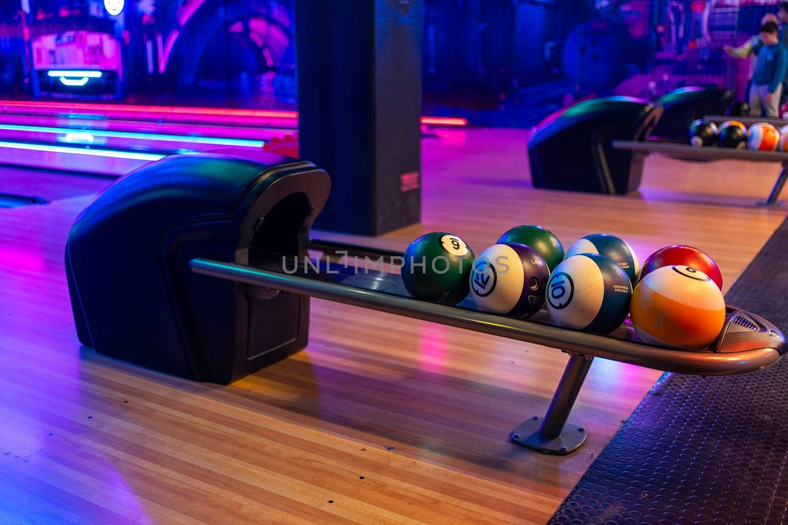Various bowling balls arranged in stand on wooden lane at bowling hall. Illuminated playroom in shopping center with no people