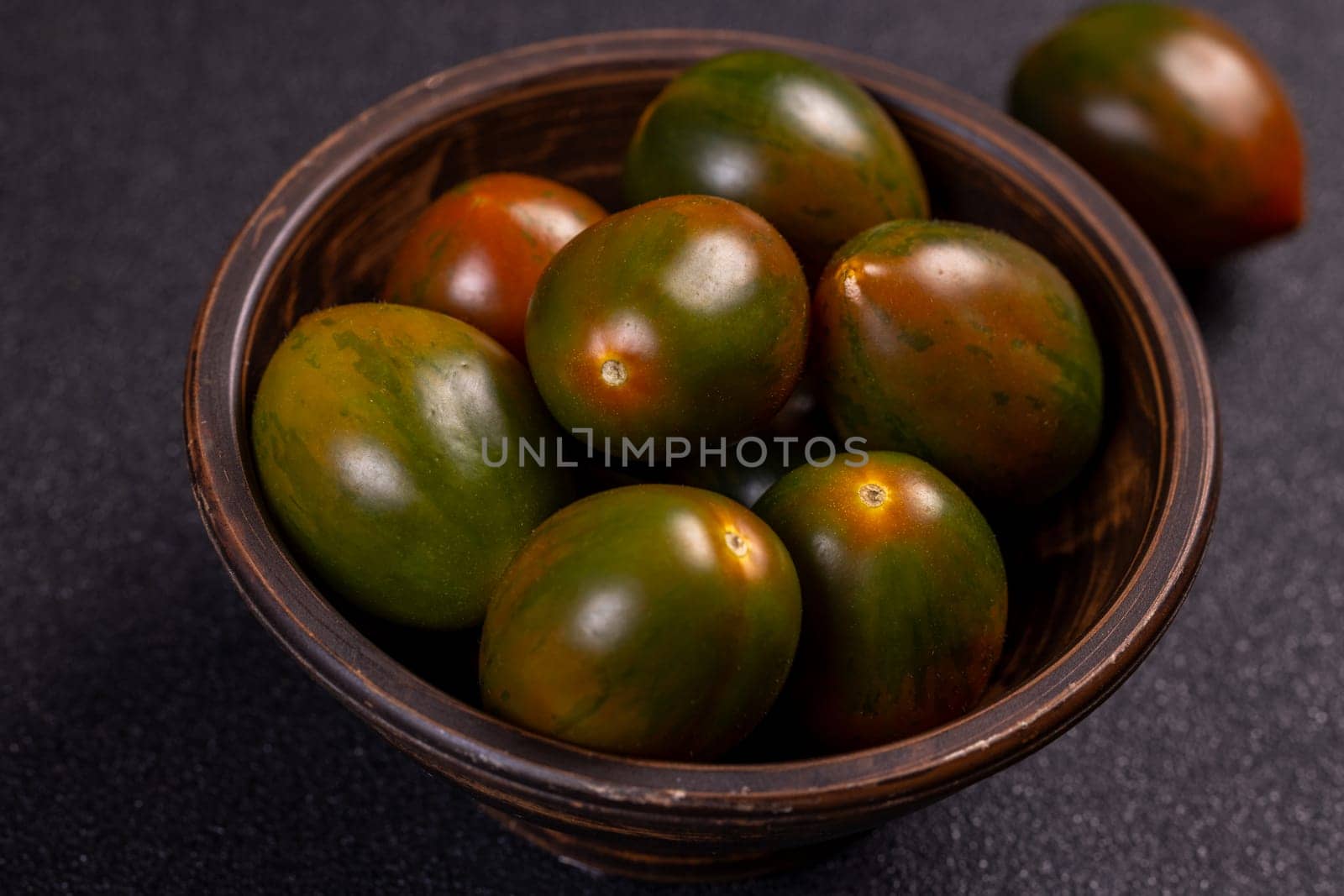 Fresh, ripe kumato tomatoes are displayed in a rustic bowl, showcasing their unique dark green and reddish brown hues against a dark background