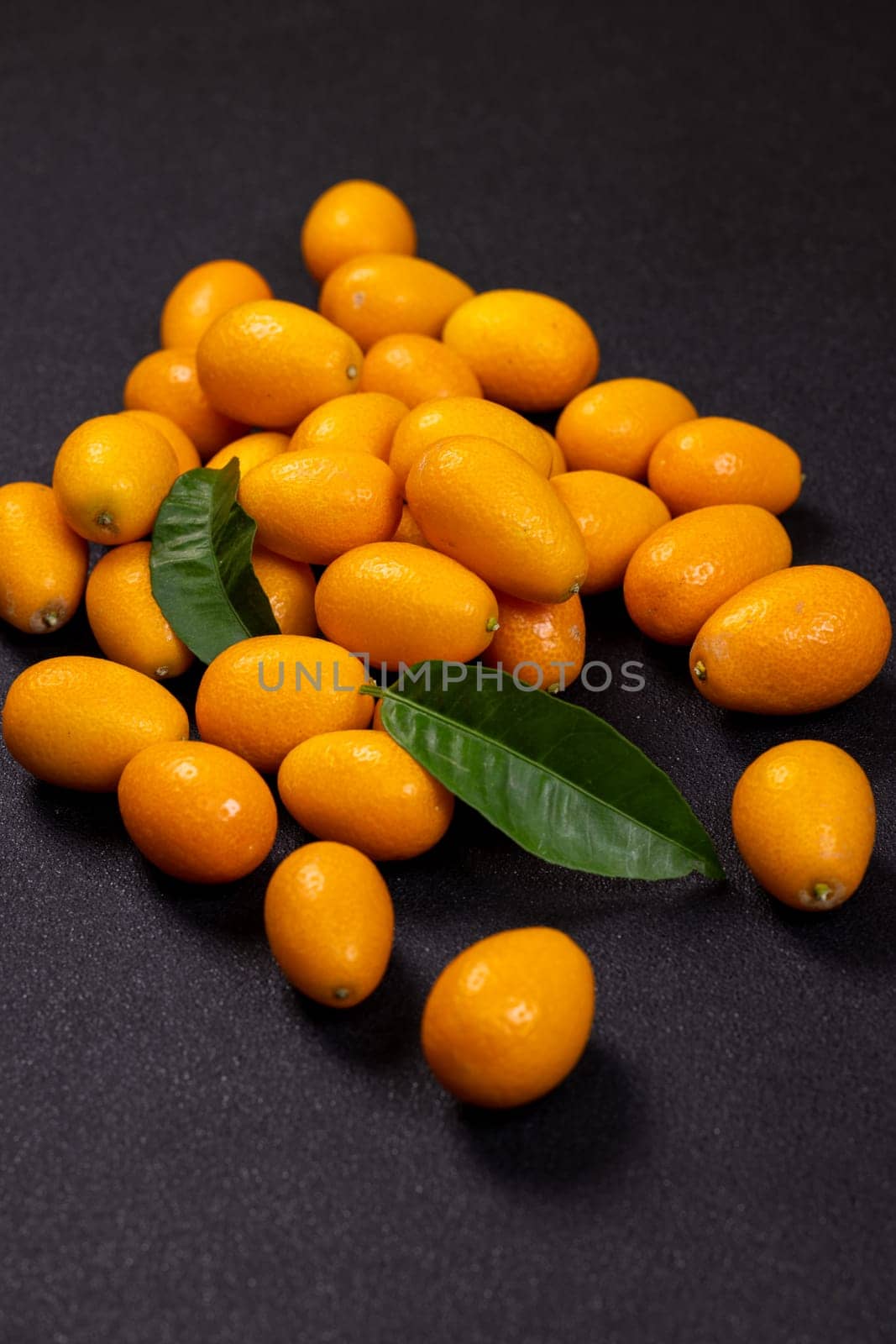 Fresh kumquat fruits nestled among vibrant green leaves create a striking display against a dark background, highlighting their juicy appeal