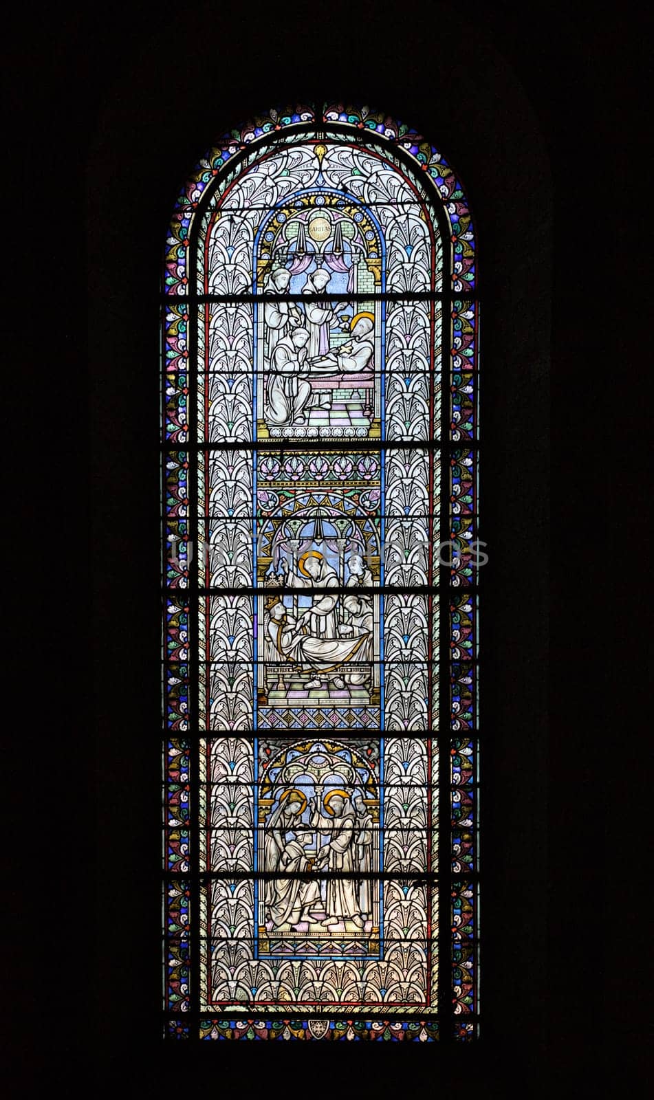 Intricate stained glass window illuminates the interior of Saint-Sernin basilica with vibrant biblical narratives.