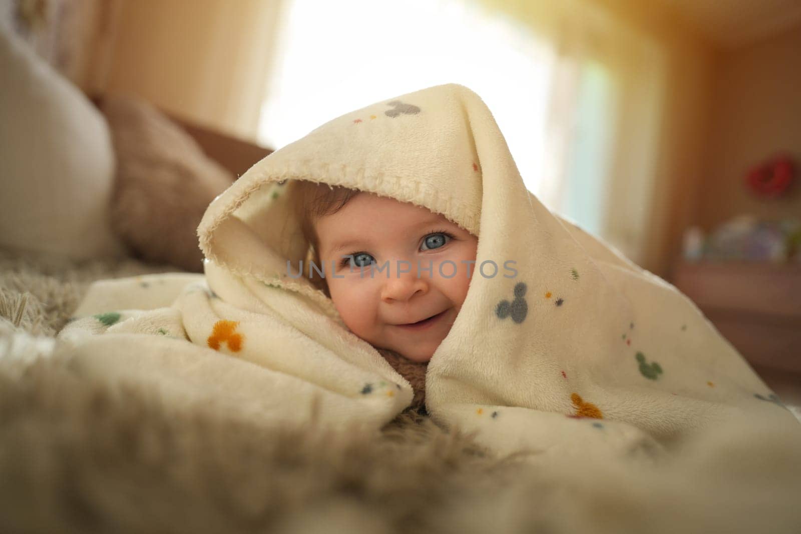 Smiling baby girl crawling on bed under the blanket. Adorable kid portrait. 6 month old child. Childhood concept. High quality photo