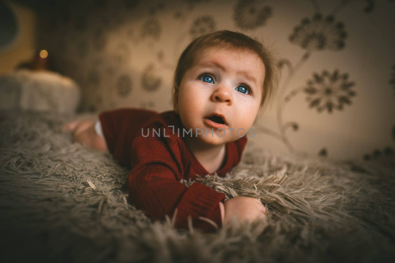 Blue-eyed baby girl in red clothes close up crawling on bed. Adorable kid portrait. 5 month old child. Childhood concept. High quality photo