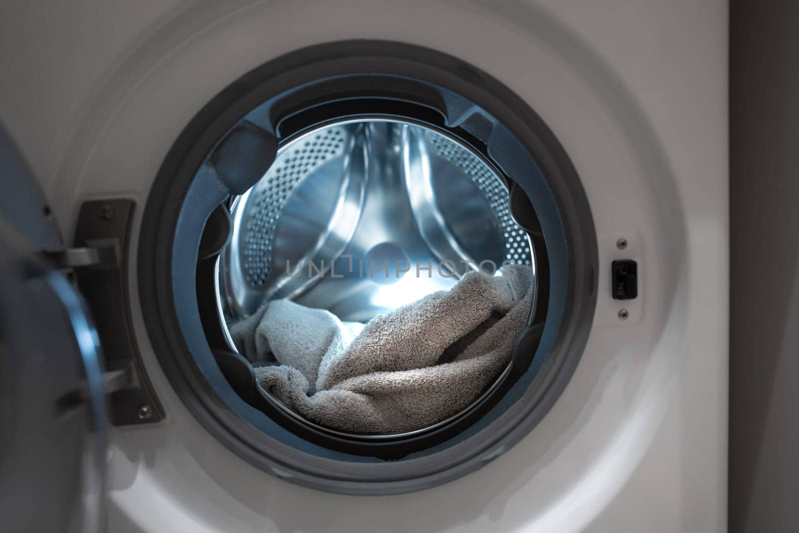 Opened washing machine drum with towel. Closeup. Front view. Washing dirty clothes in the washer. High quality photo