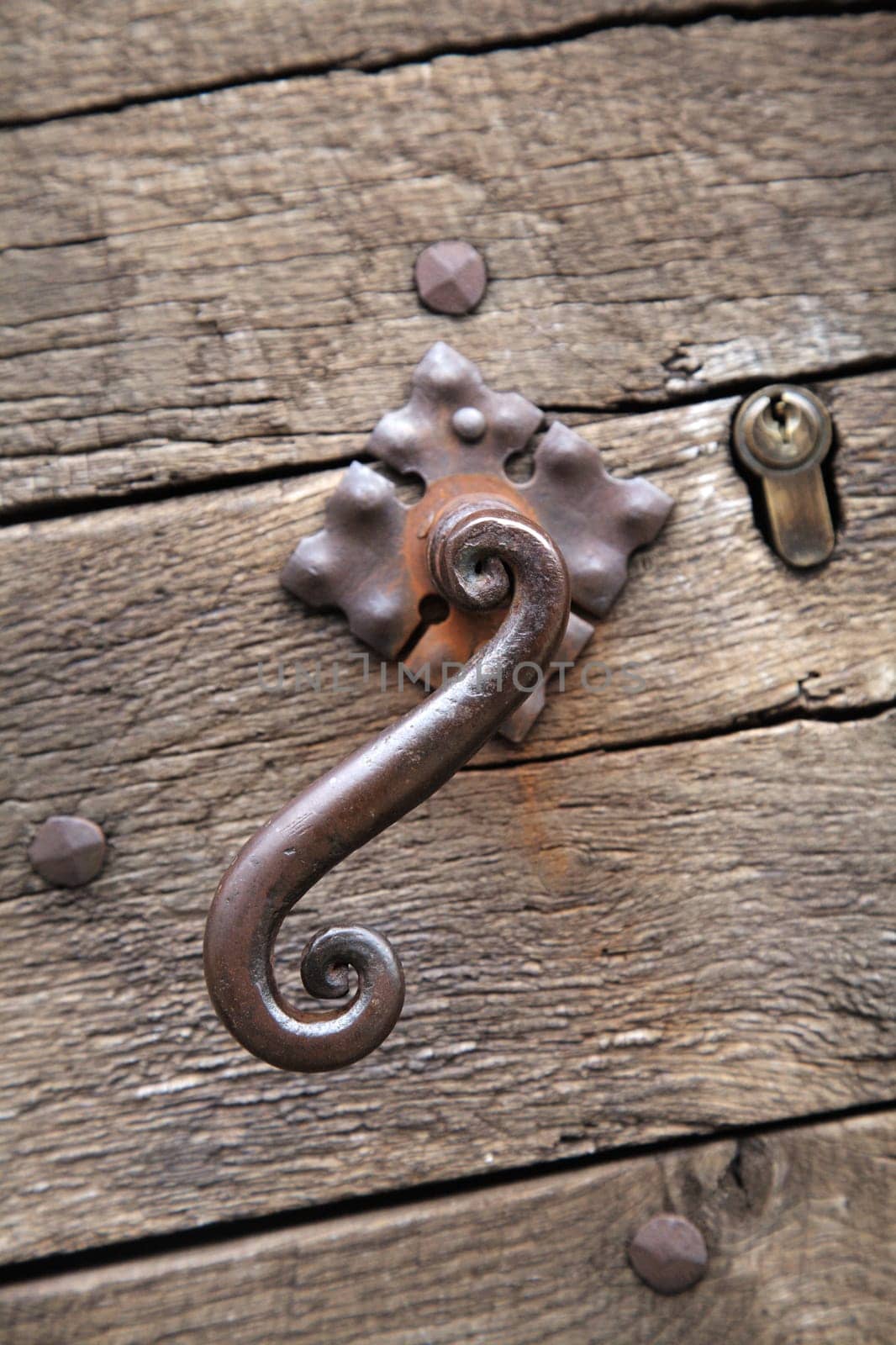 Close-up view of an ornate metal latch on a rustic wooden door in Sarlat-la-Caneda, highlighting local artisan skills.
