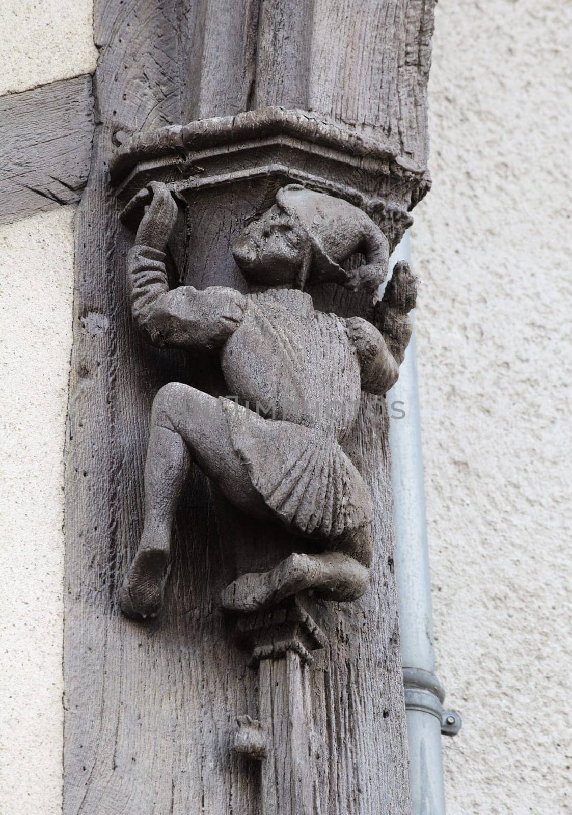 A unique wooden sculpture of a figure climbing a pillar adorns a historic building in Blois, France.
